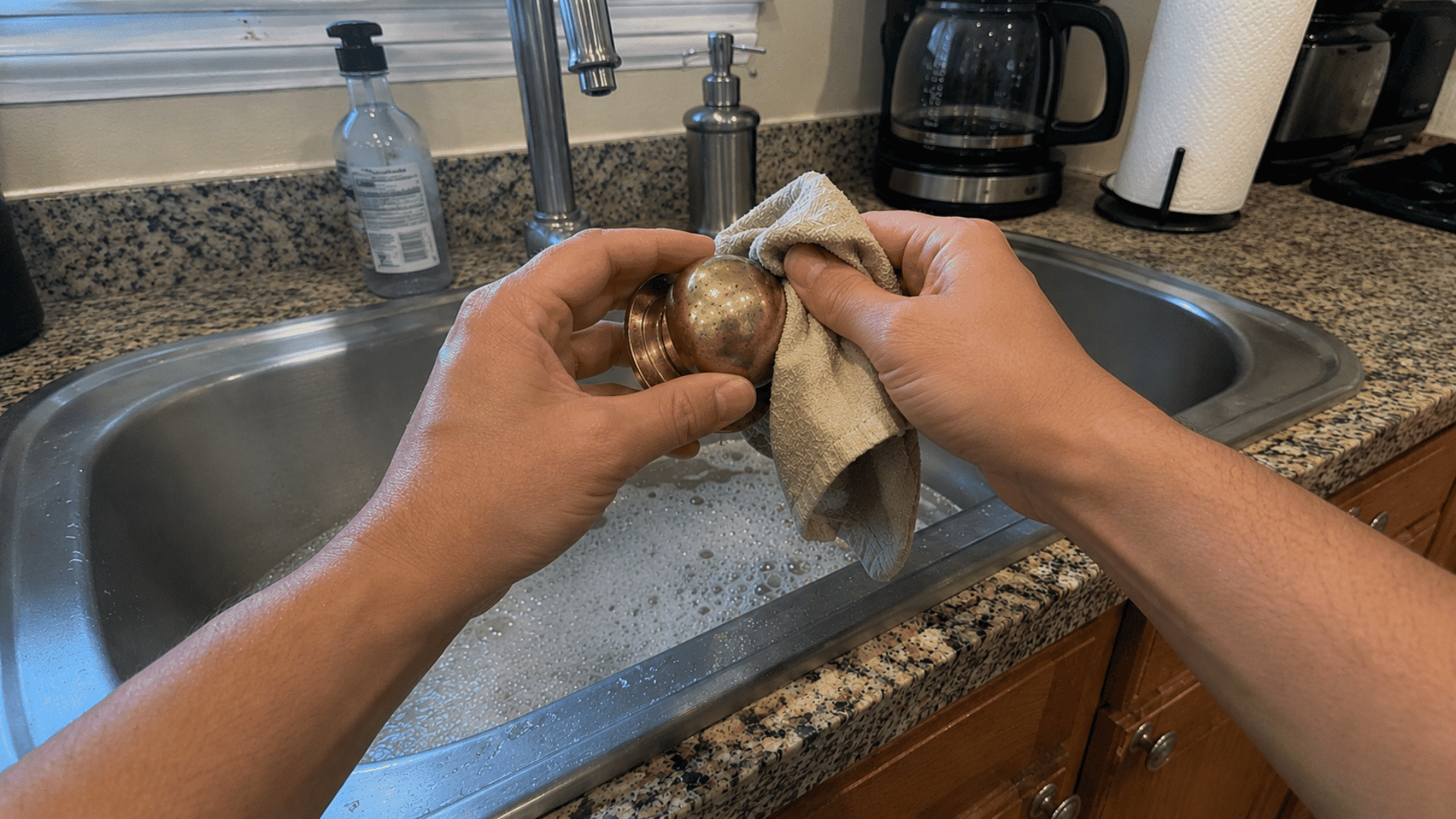 hands wiping a brass doorknob with a soapy cloth over a bowl of warm water