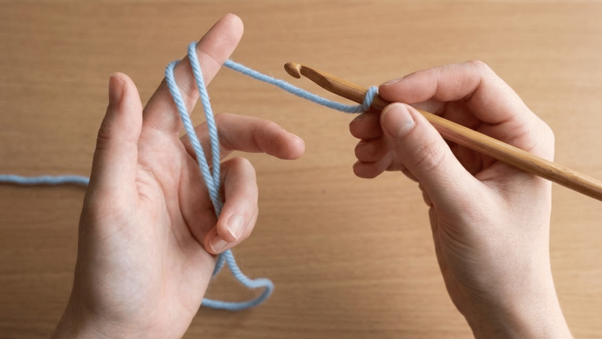 hands holding a wooden crochet hook and light blue yarn in the correct beginner grip