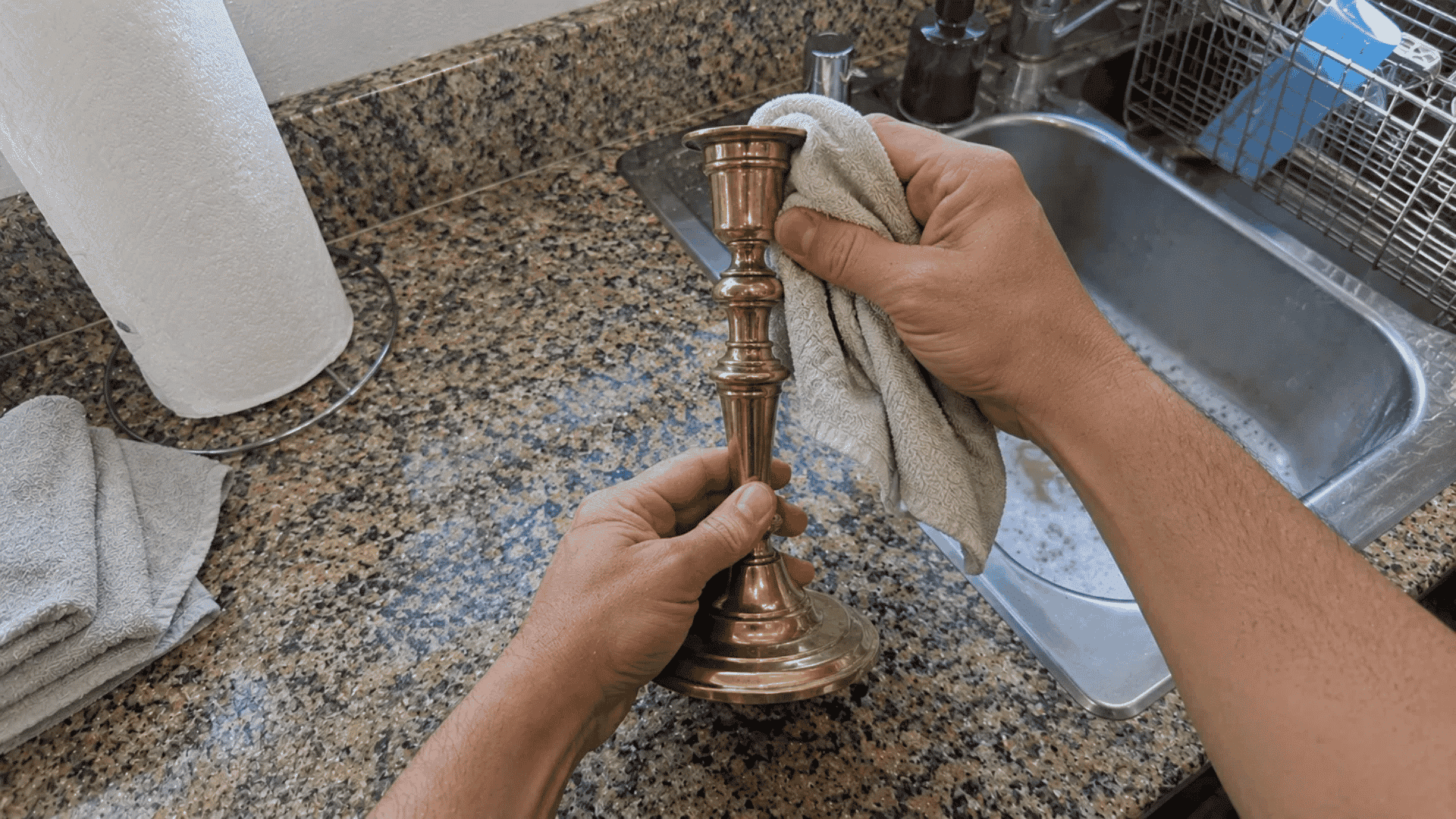 hands holding a brass candlestick base while wiping the stem with a cloth