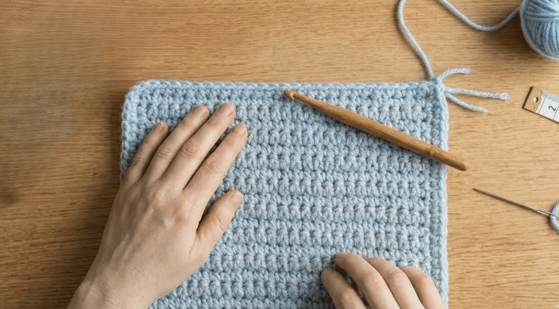 hands pulling yarn tail through last loop to fasten off crochet swatch