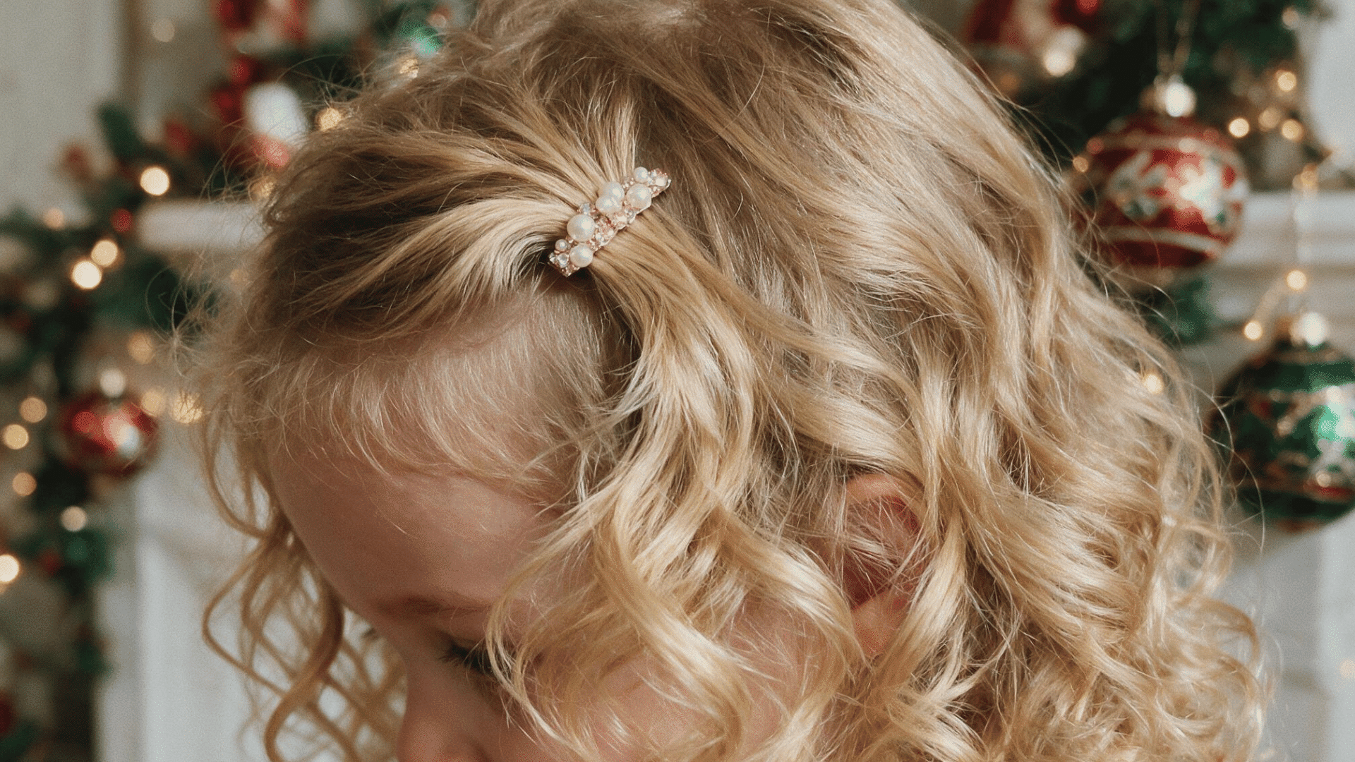 little girl with soft curly hair styled with a pearl hair clip in front of a decorated christmas tree