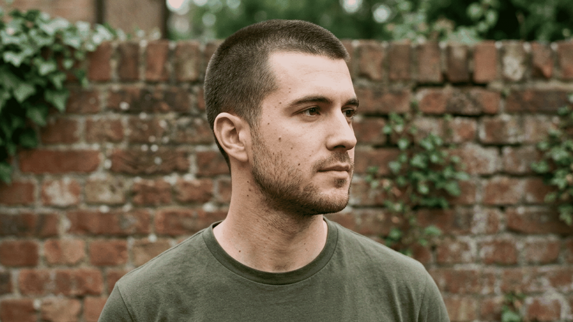 man with an oval face wearing an even length butch cut and light stubble