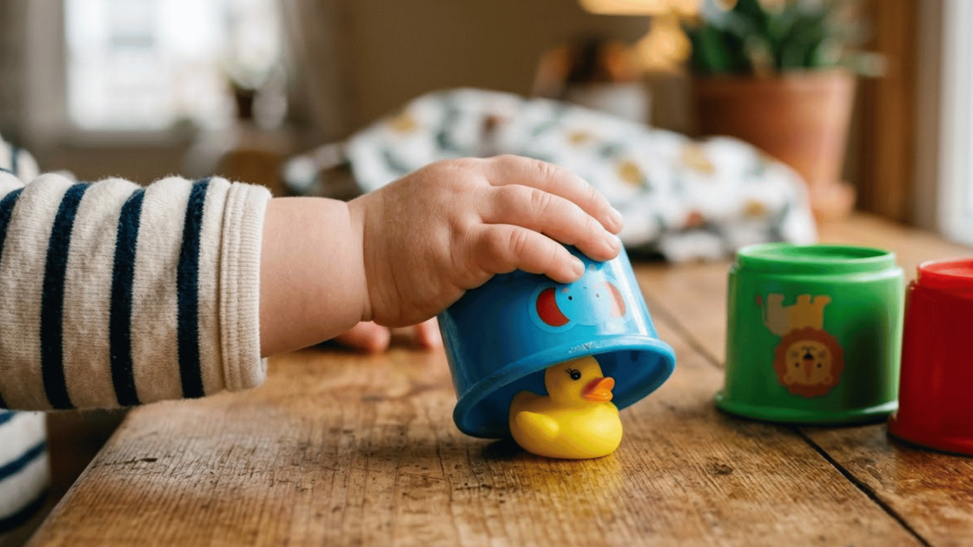 toddler hand lifts a cup to reveal a hidden toy in a peekaboo game