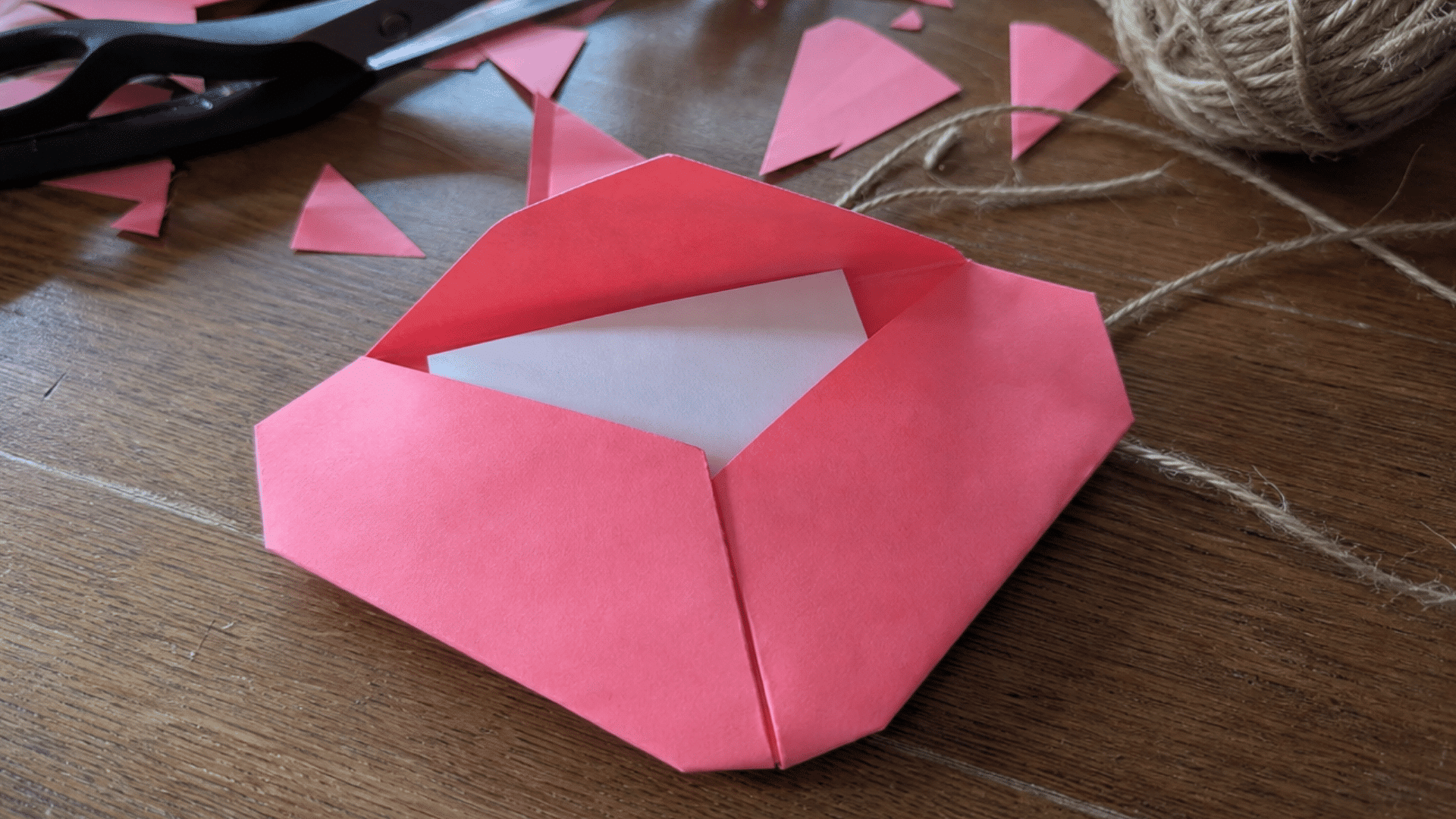 pink folded paper heart envelope with a blank note inside on a wooden table