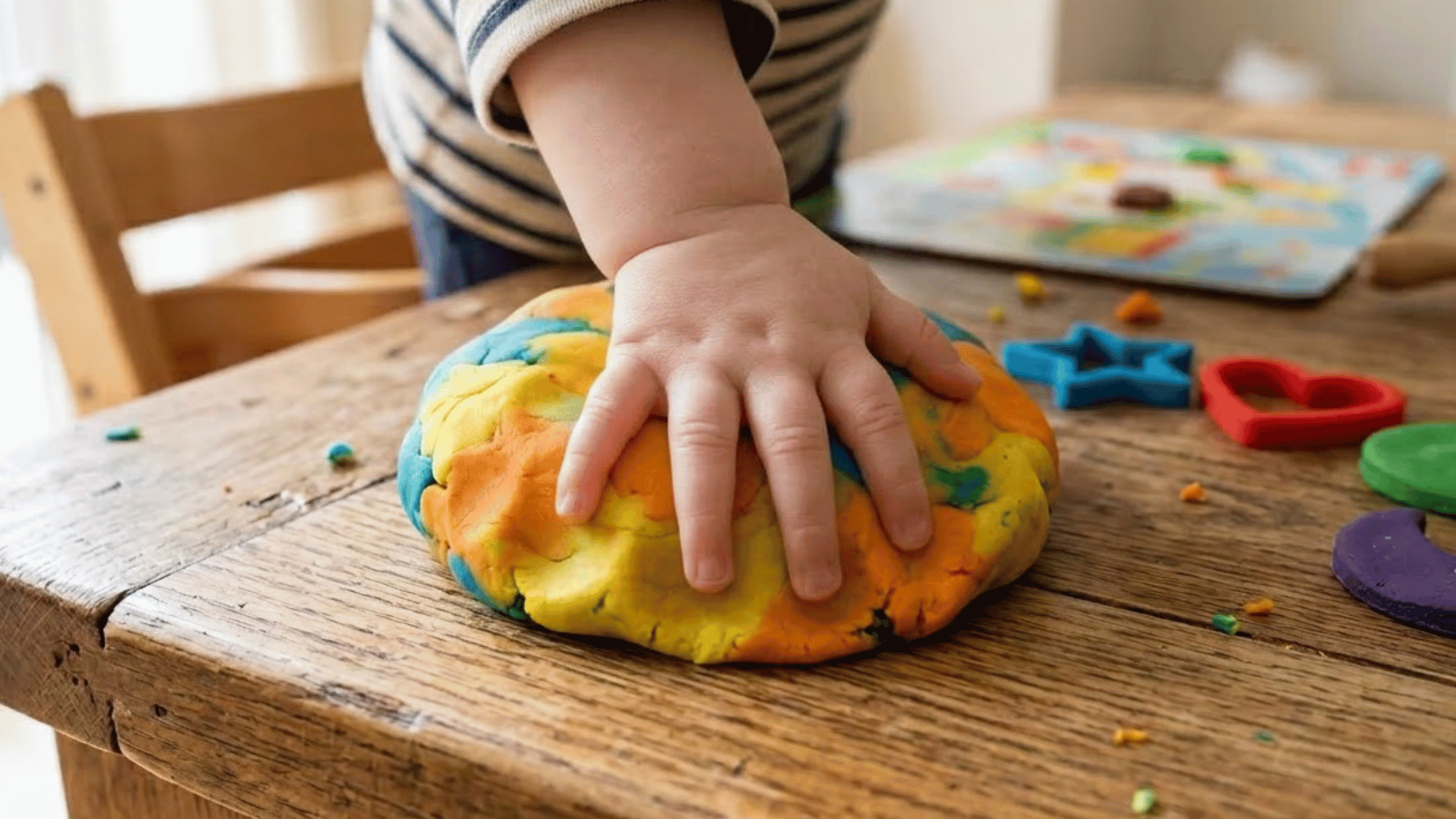 toddler hand presses flat into a ball of soft playdough on a wooden table