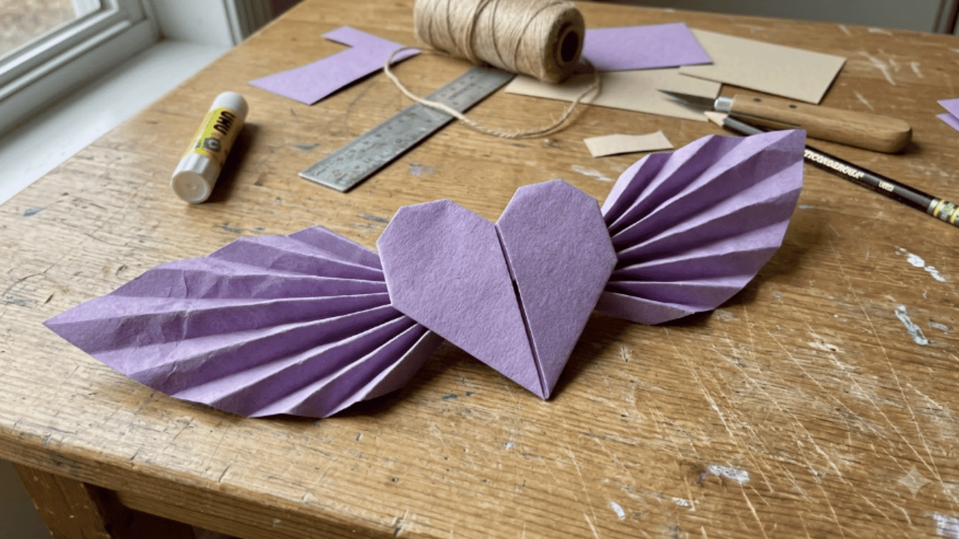 purple folded paper heart with wide wings displayed on a diy craft table