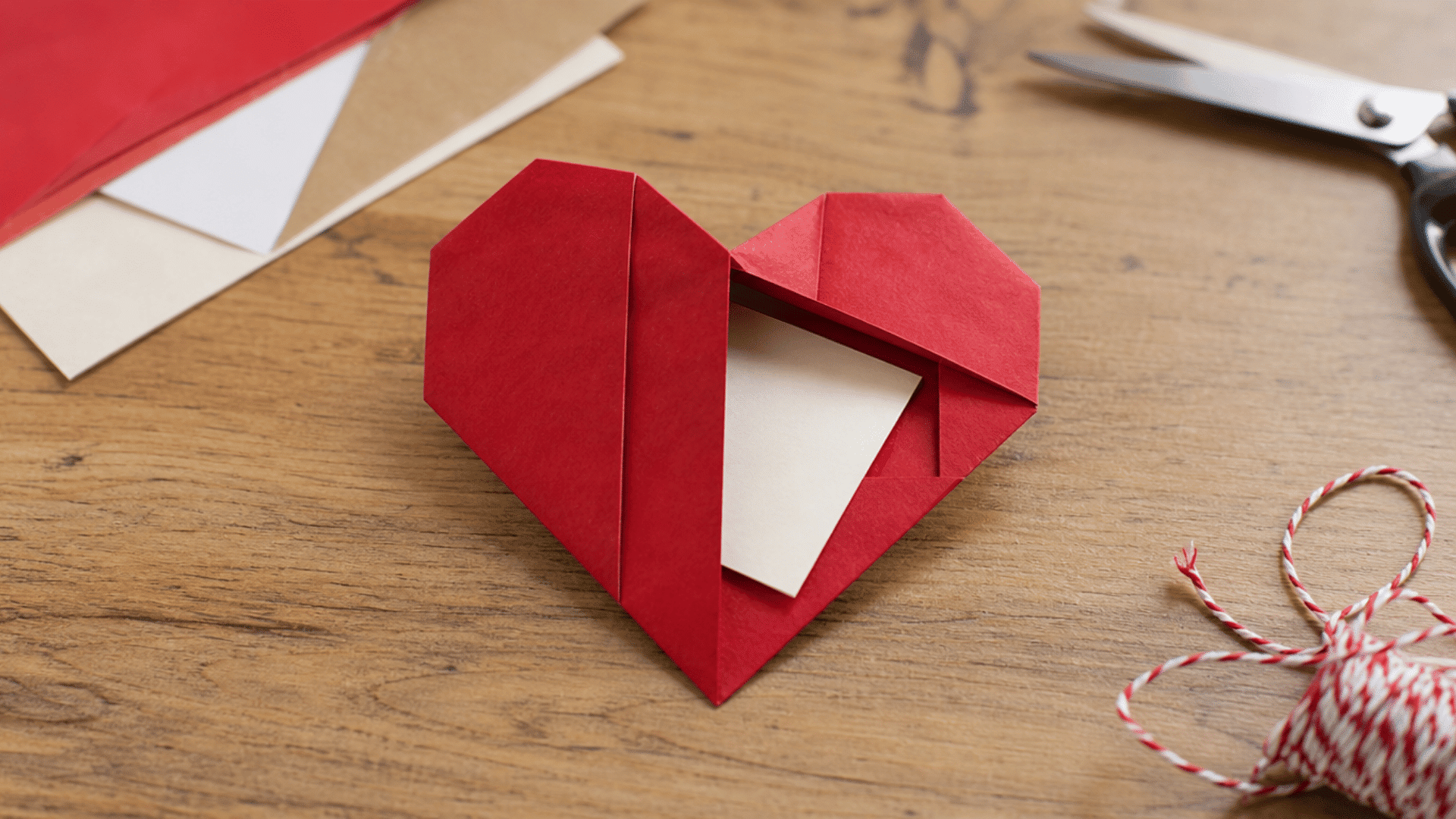 red folded paper heart with hidden pocket holding a blank note on a craft table