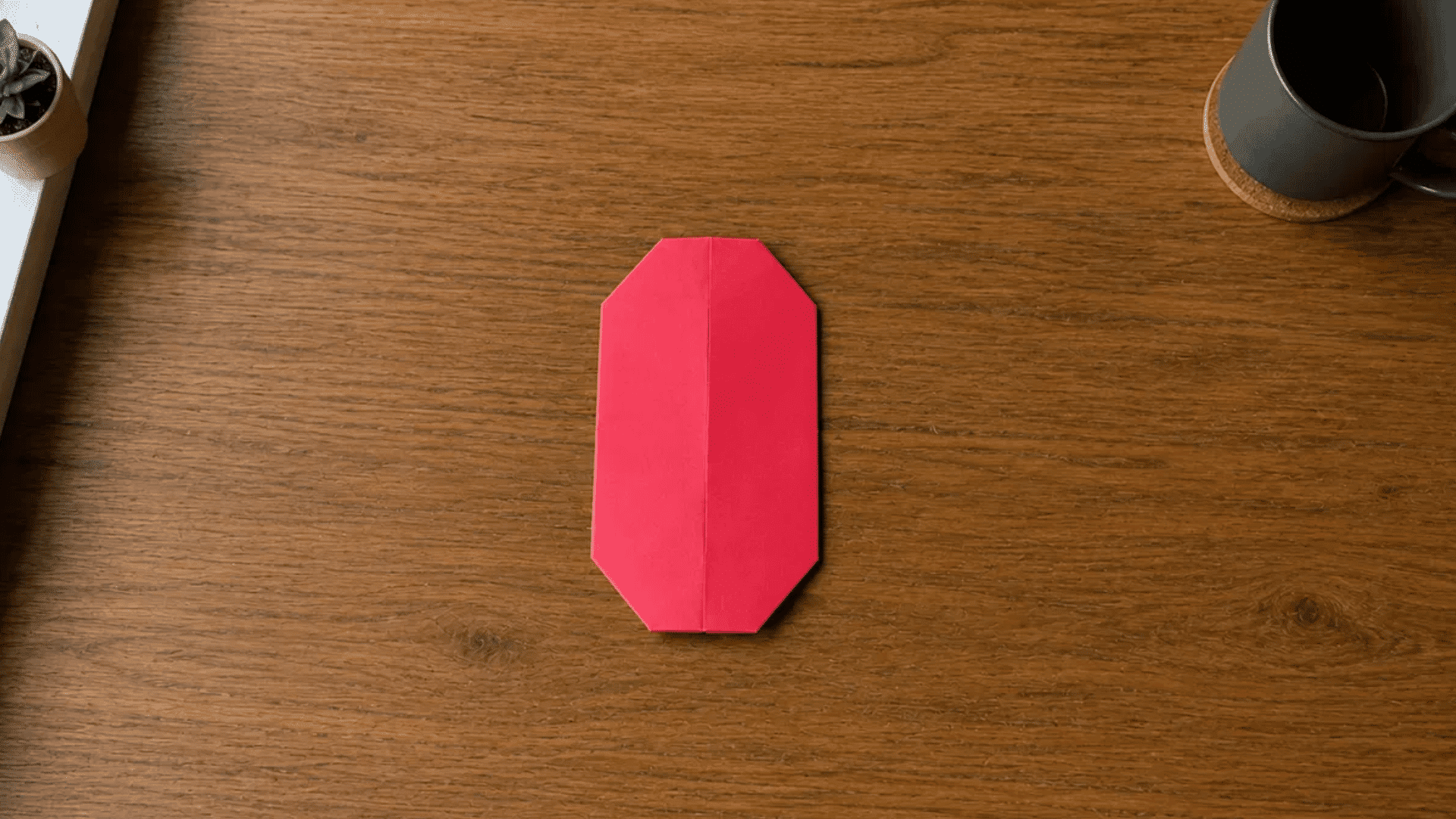 red paper folded into an elongated shield shape for an origami heart tutorial