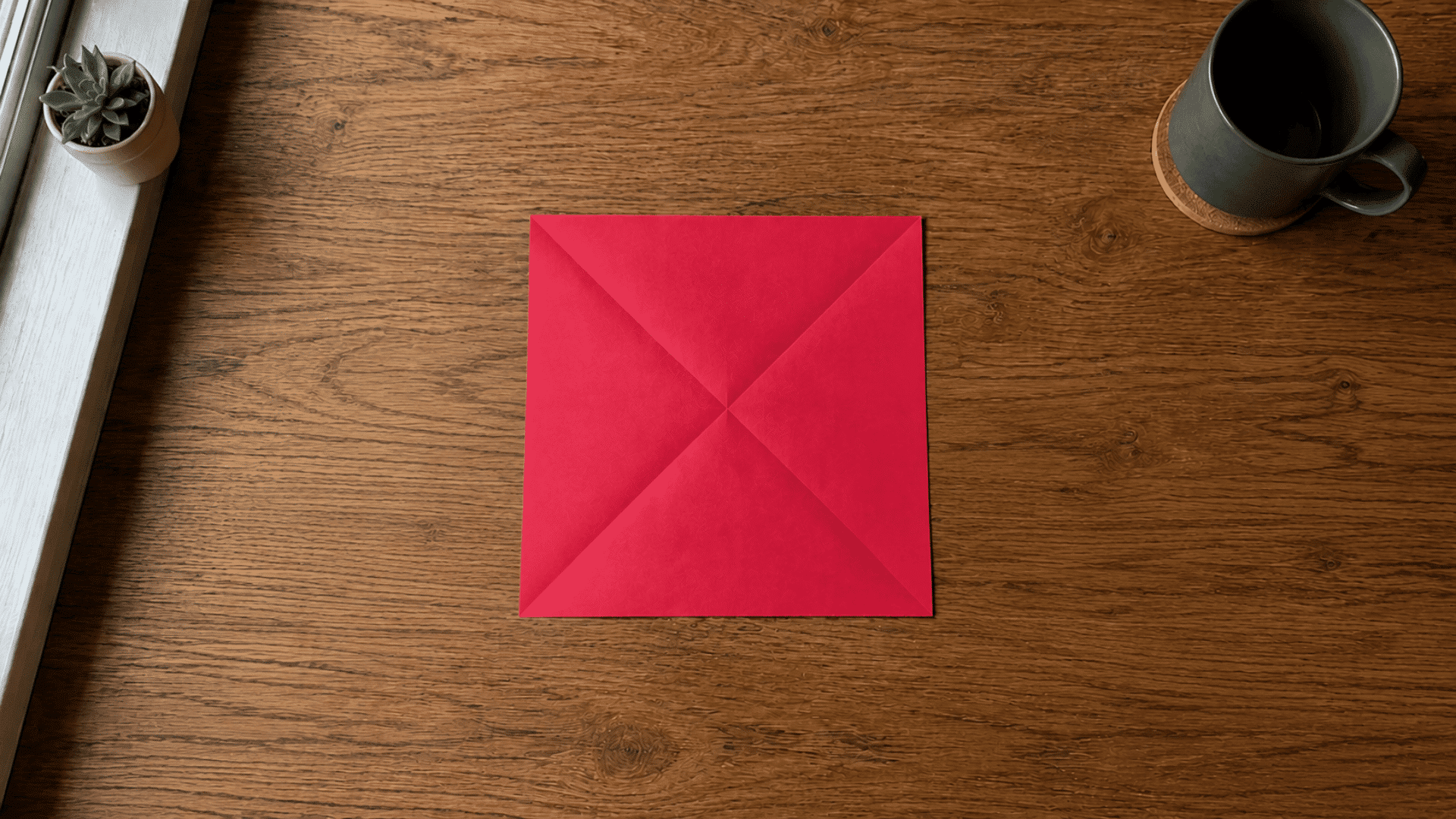red square paper folded diagonally to make the first creases for an origami heart