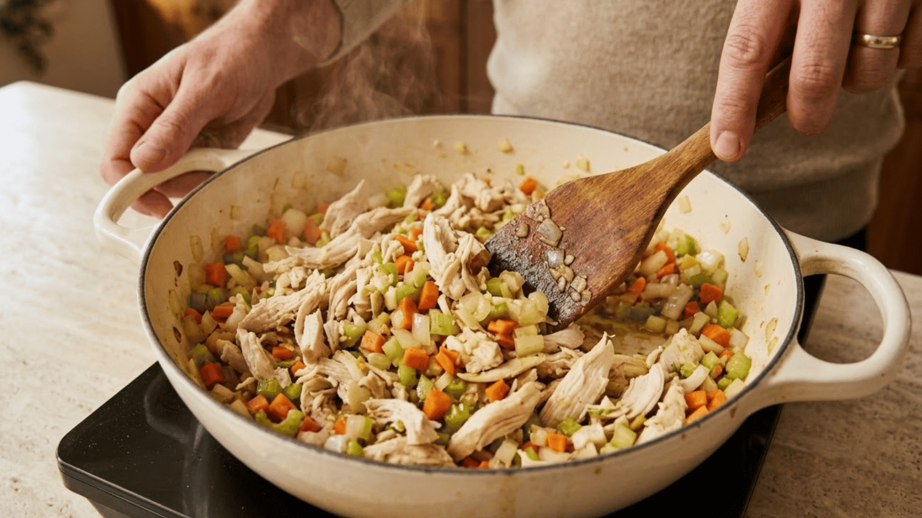 shredded chicken, garlic, carrots, celery, and onion sautéing in a cast iron skillet for chicken pot pie filling
