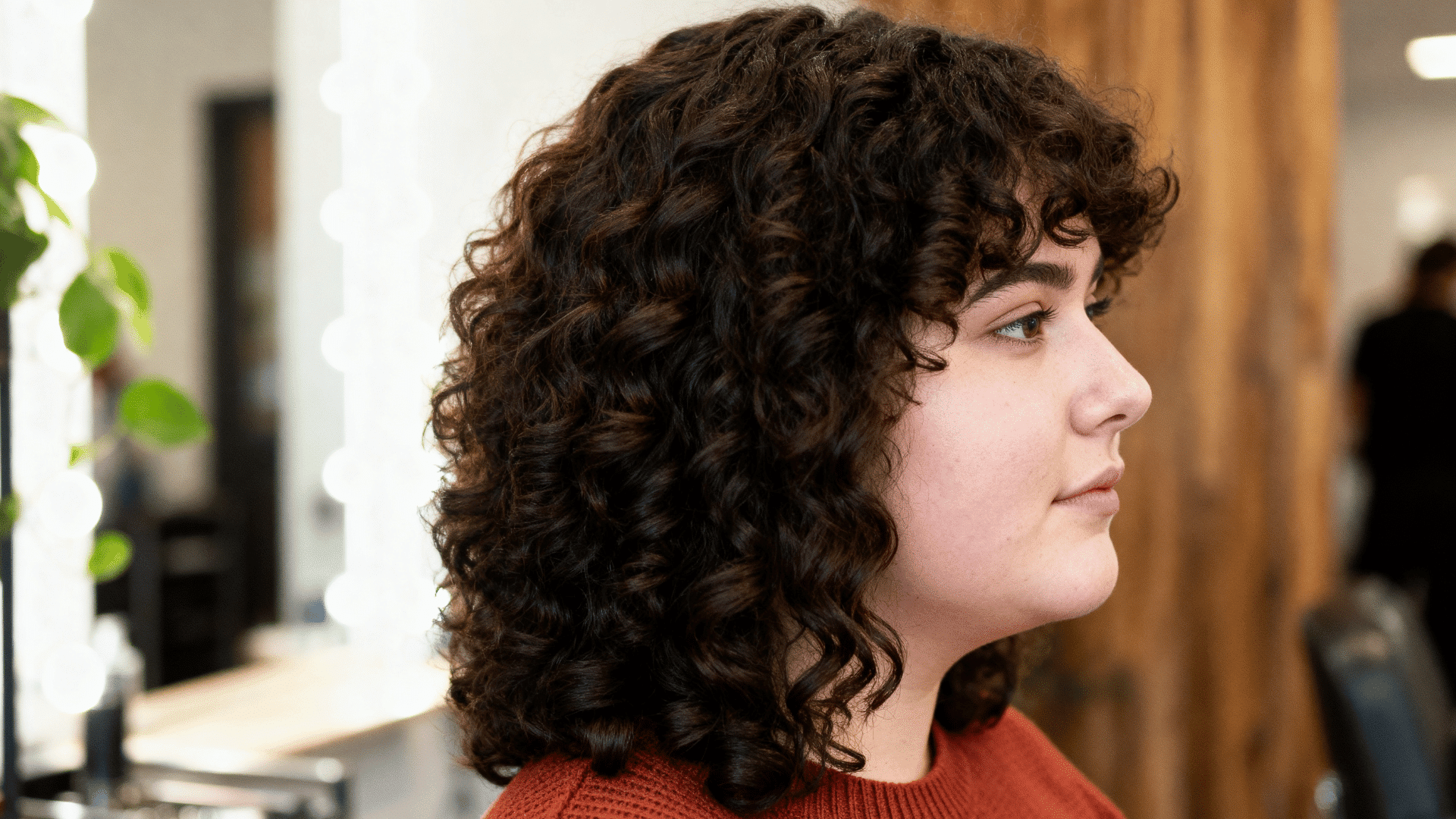 side-profile photo of a woman with thick curly dark brown hair styled in a natural medium-length curly haircut