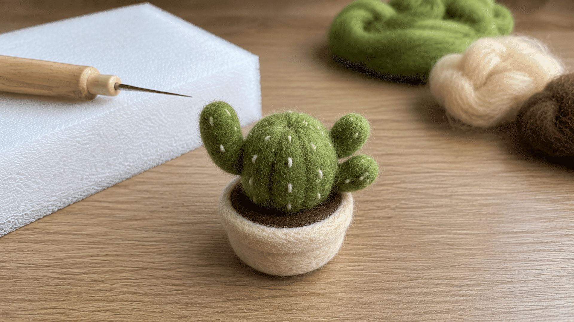 Small felted green cactus with arms in a white pot, felting needle nearby