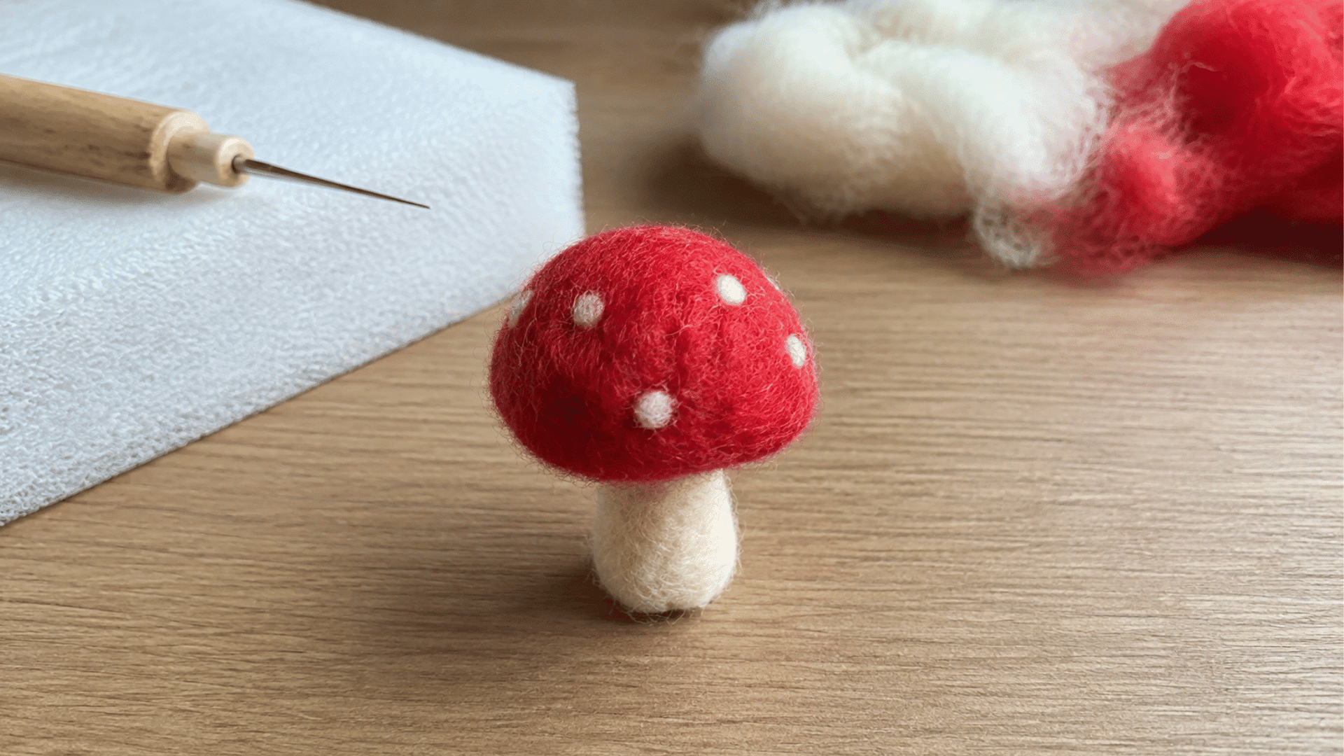 Small felted mushroom with red spotted cap and white stem, felting needle nearby