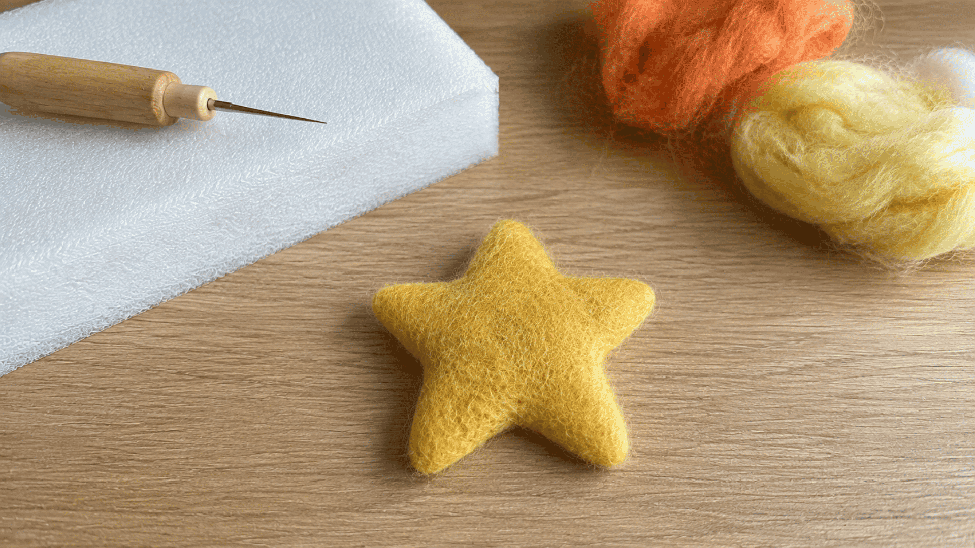 Small felted yellow star shape on wooden table with felting needle and wool roving