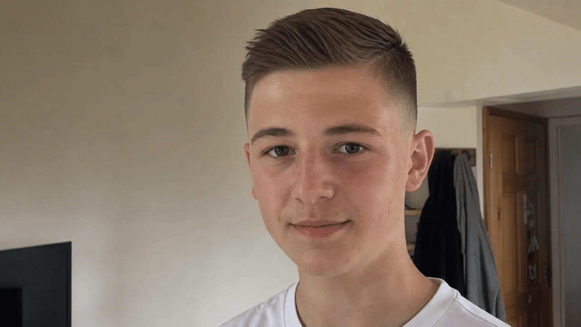 smiling teen boy with side part crew cut and fade blend hairstyle standing indoors at home