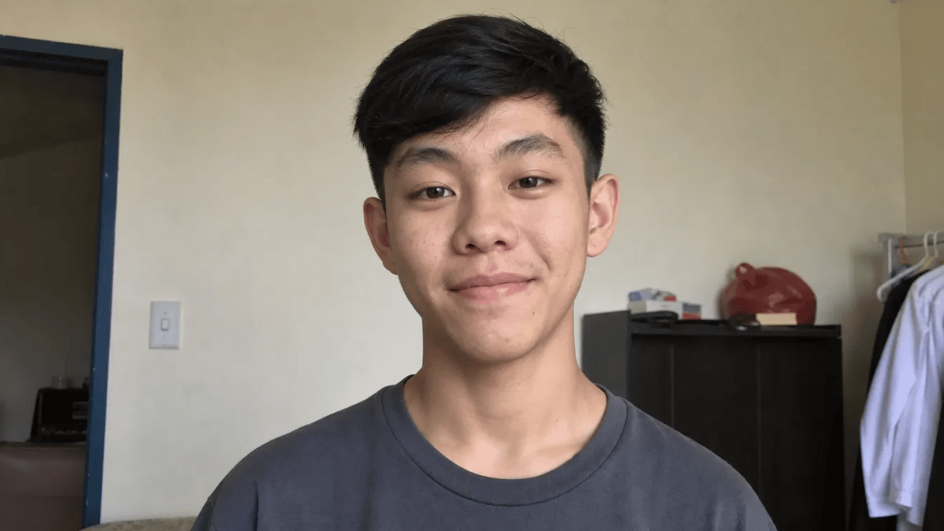 smiling young man with side-swept crew cut hairstyle standing indoors near open doorway