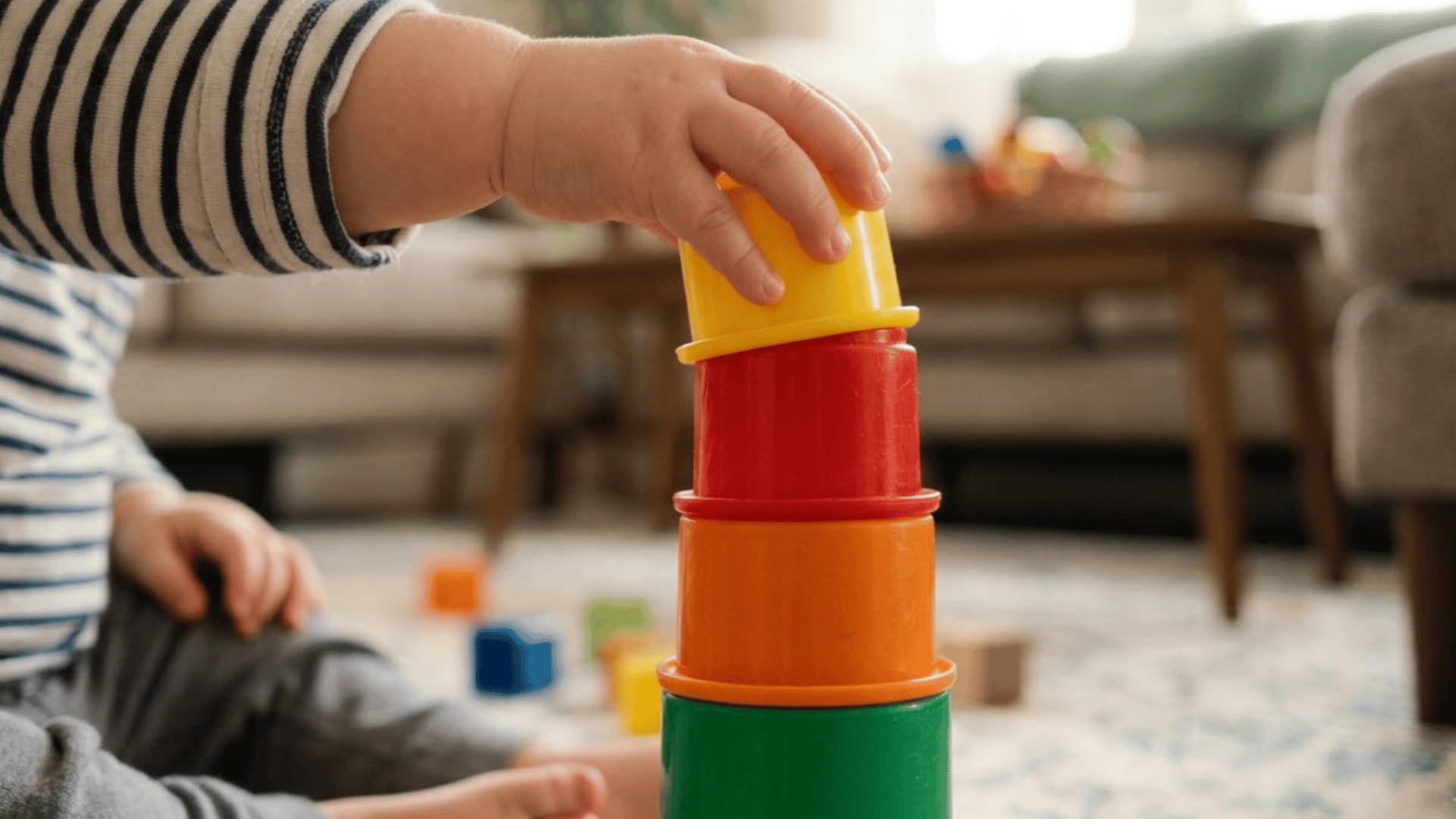 toddler hand places a colorful stacking cup on top of a growing tower