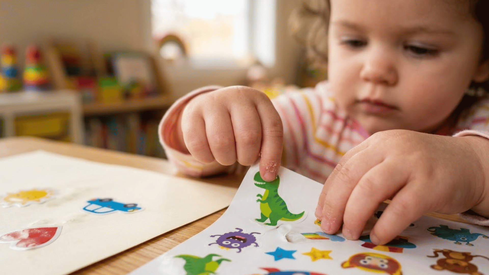 toddler fingers peel a large sticker from its backing sheet on a table