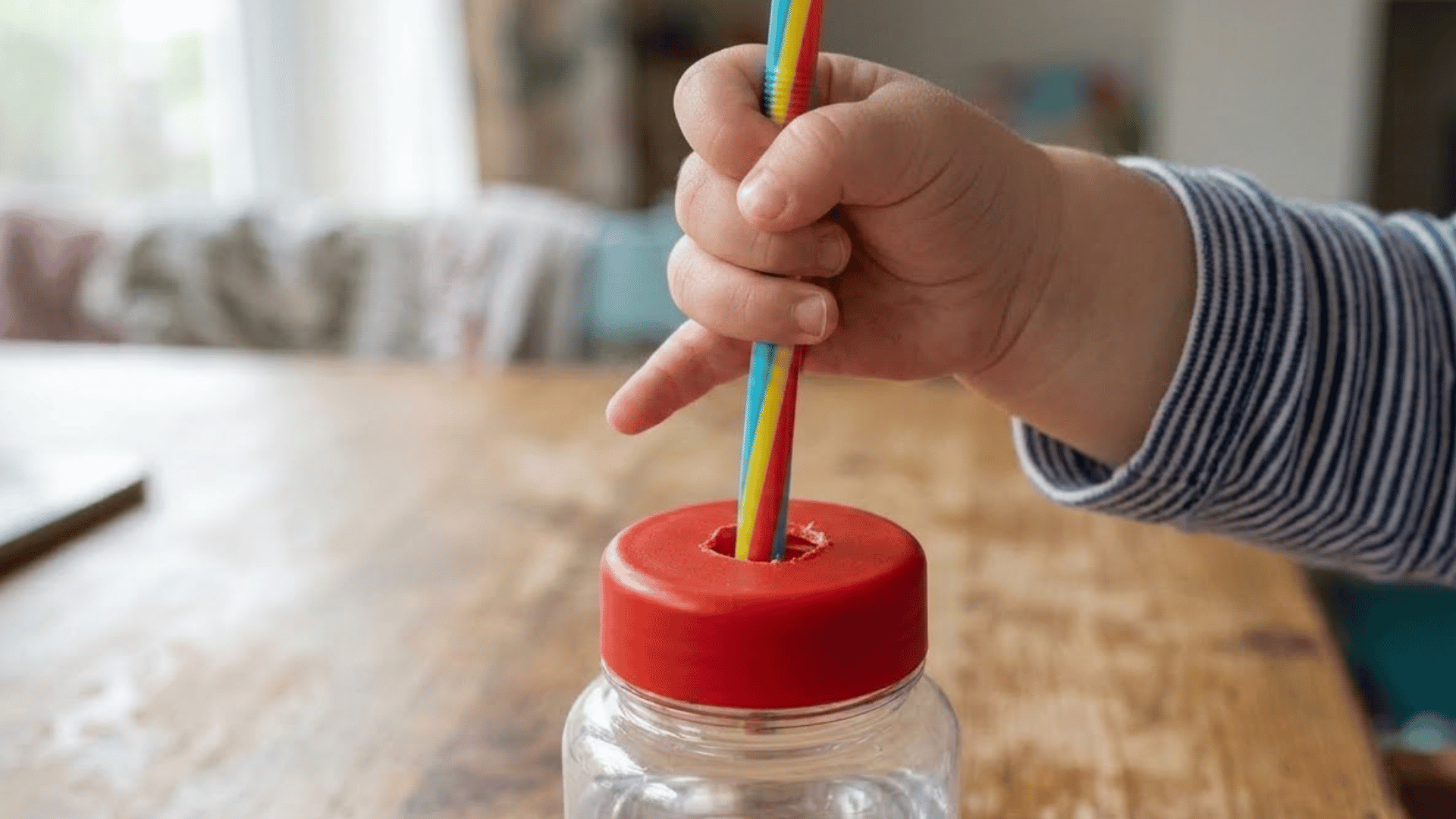 toddler hand pinches a thick straw above a bottle with a hole in the lid