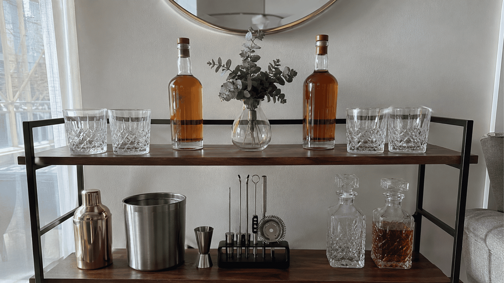 Symmetrical bar cart with matching whiskey bottles, glasses, decanters, shaker, ice bucket, and centered vase