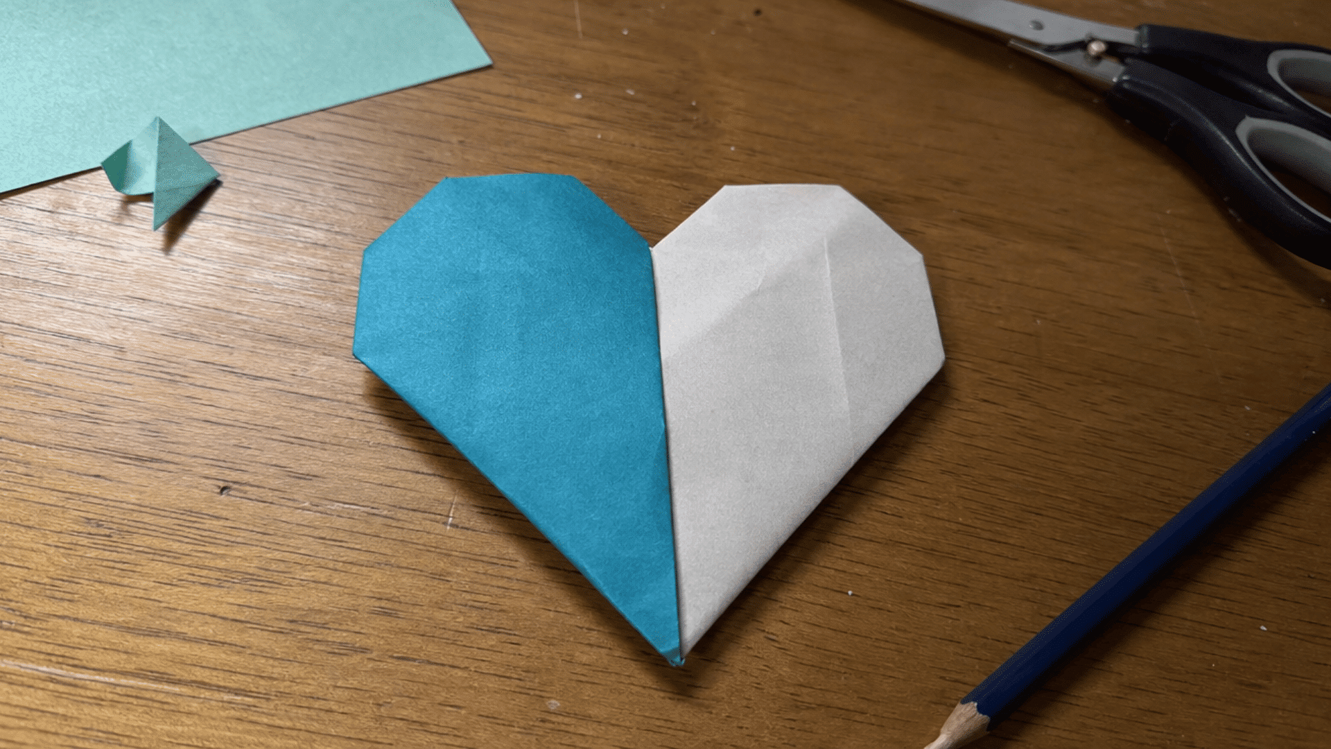 teal and white folded paper heart showing two color sections on a craft desk
