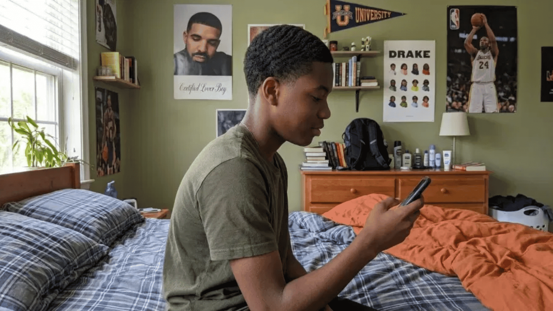 teen boy with wavy textured crew cut for thick hair using phone while sitting on bed in bedroom