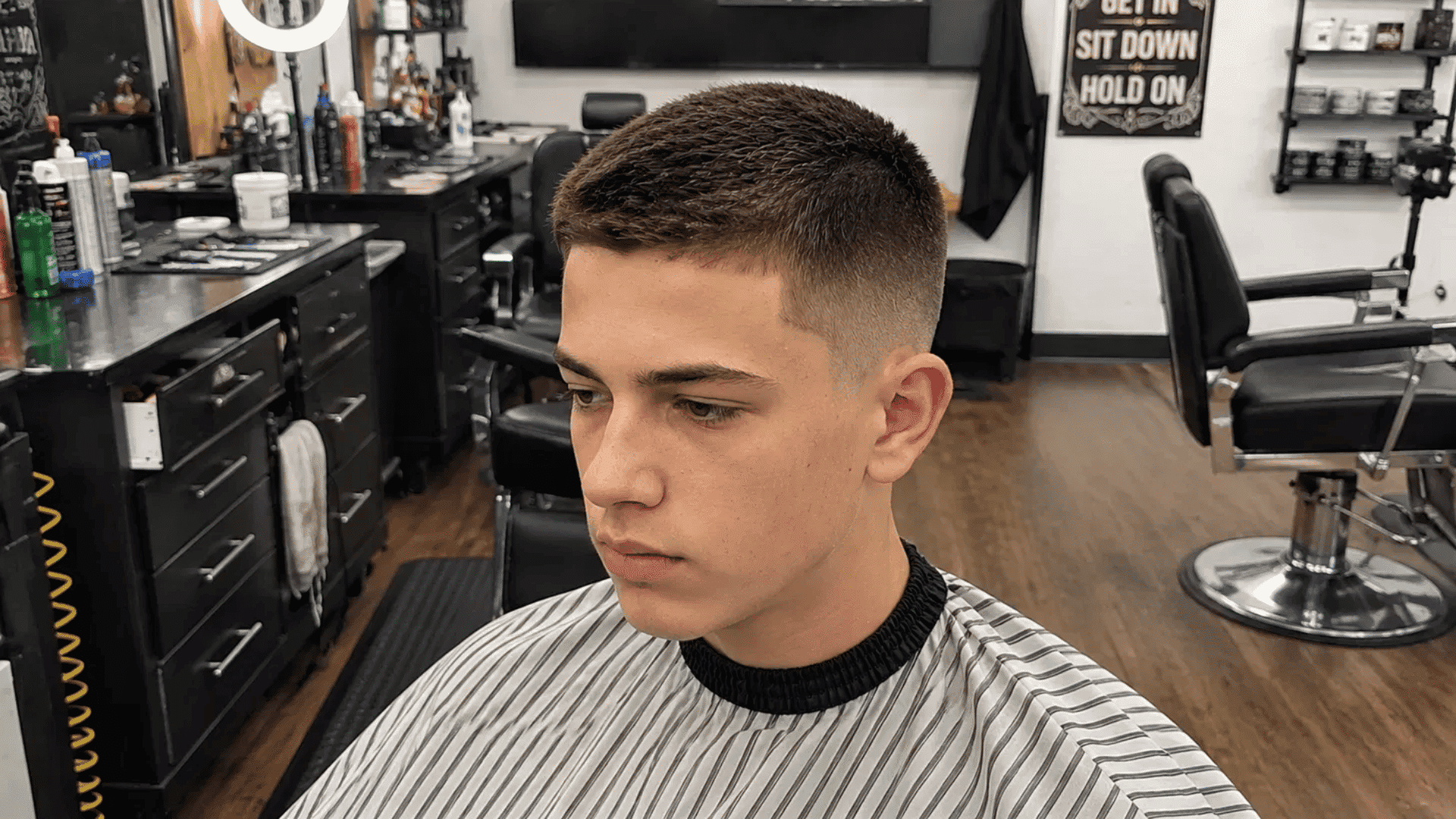 teenage boy getting short crew cut with clean sides at barbershop wearing striped hair cutting cape