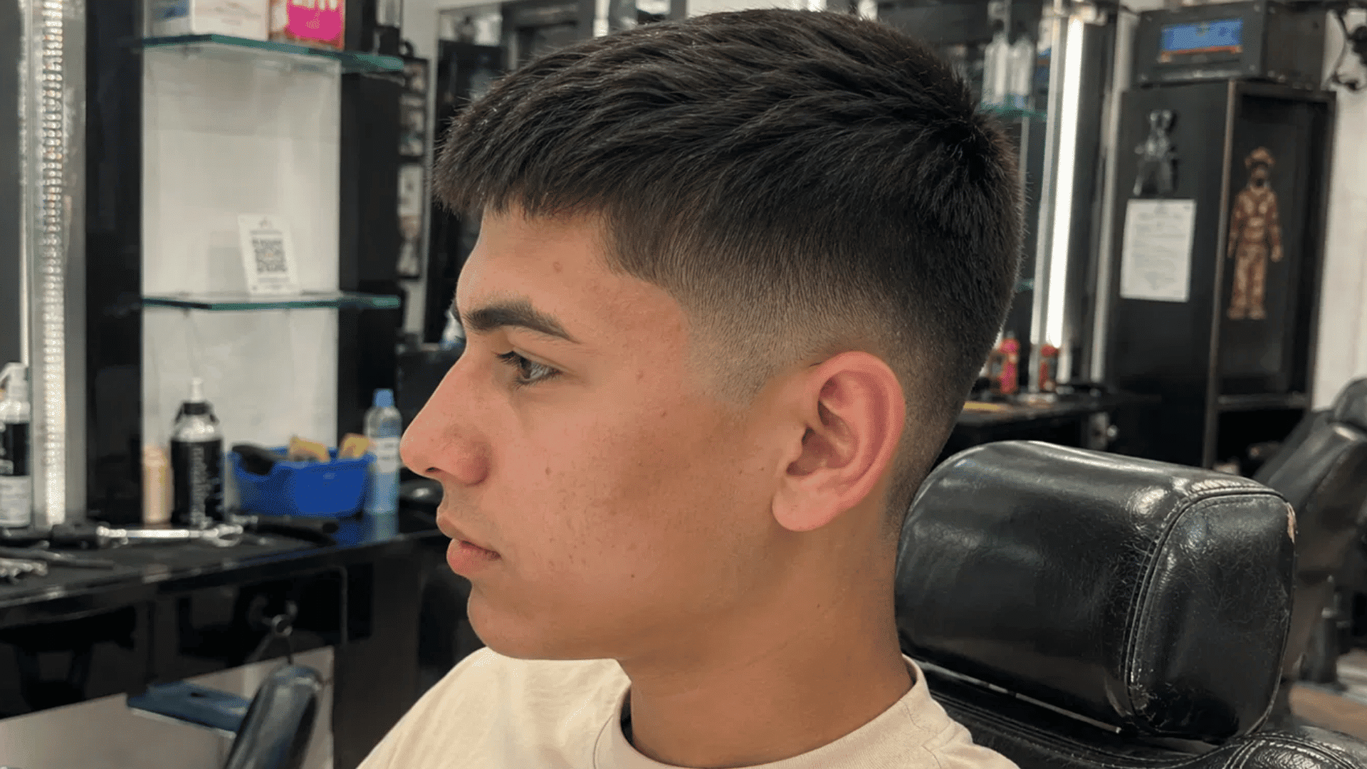 teenage boy with a classic crew cut, side profile, short neat top and faded sides, sitting in a barbershop chair
