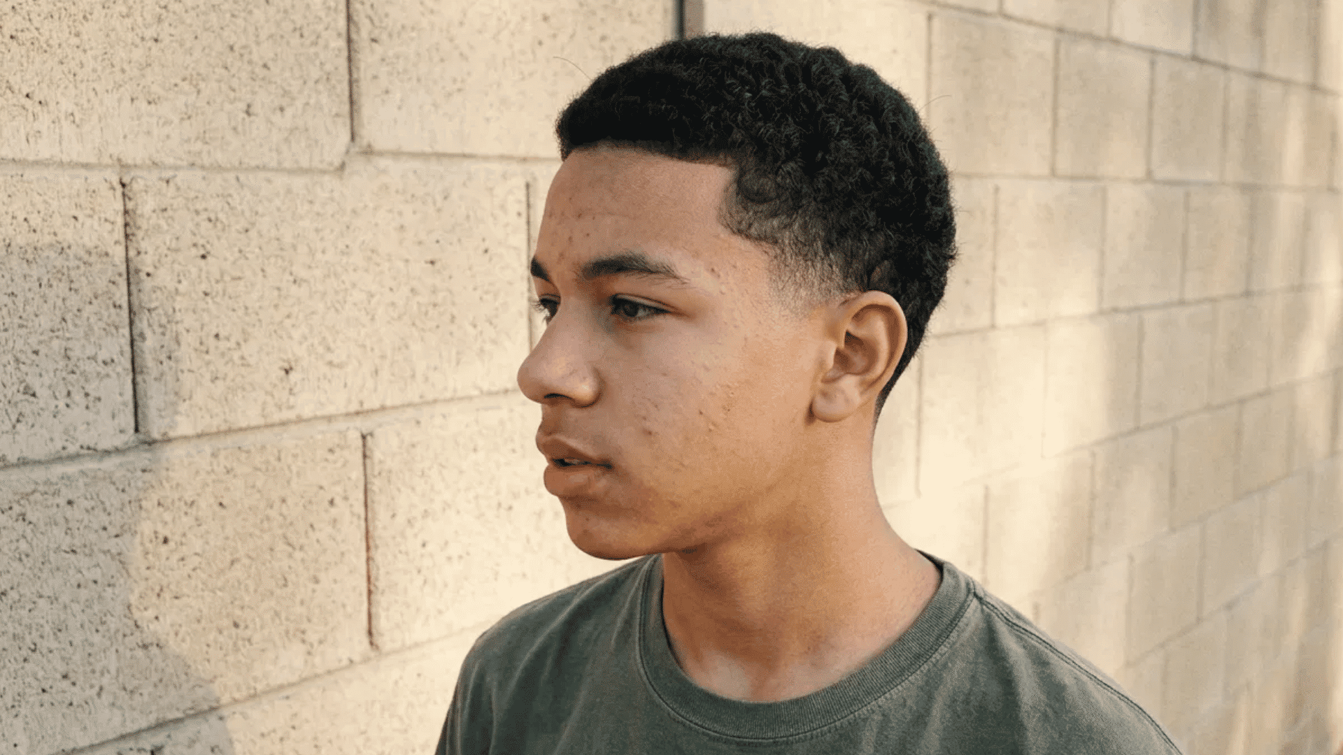 teenager displaying crew cut with rounded front hairline standing outdoors near concrete block wall