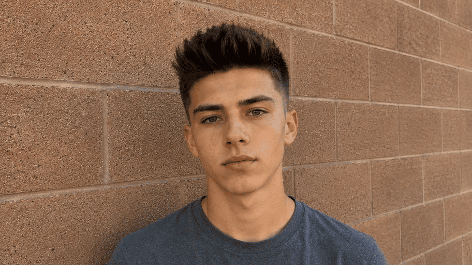 teenager posing with crew cut quiff and lifted front hairstyle leaning against brick wall