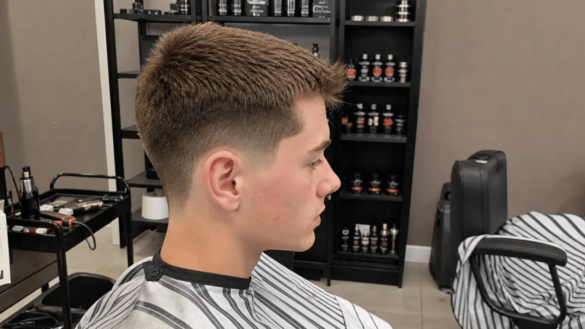 teenager showing crew cut with tapered neckline while getting haircut inside barbershop