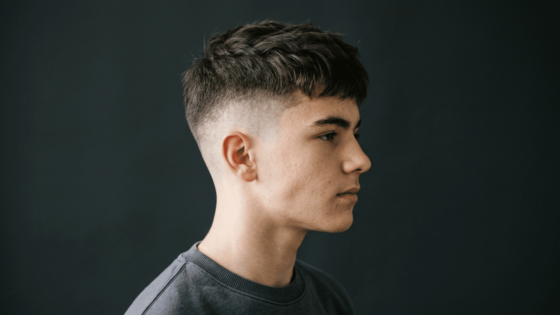 teenager showing off buzzed sides with slightly longer top haircut in profile view against dark background