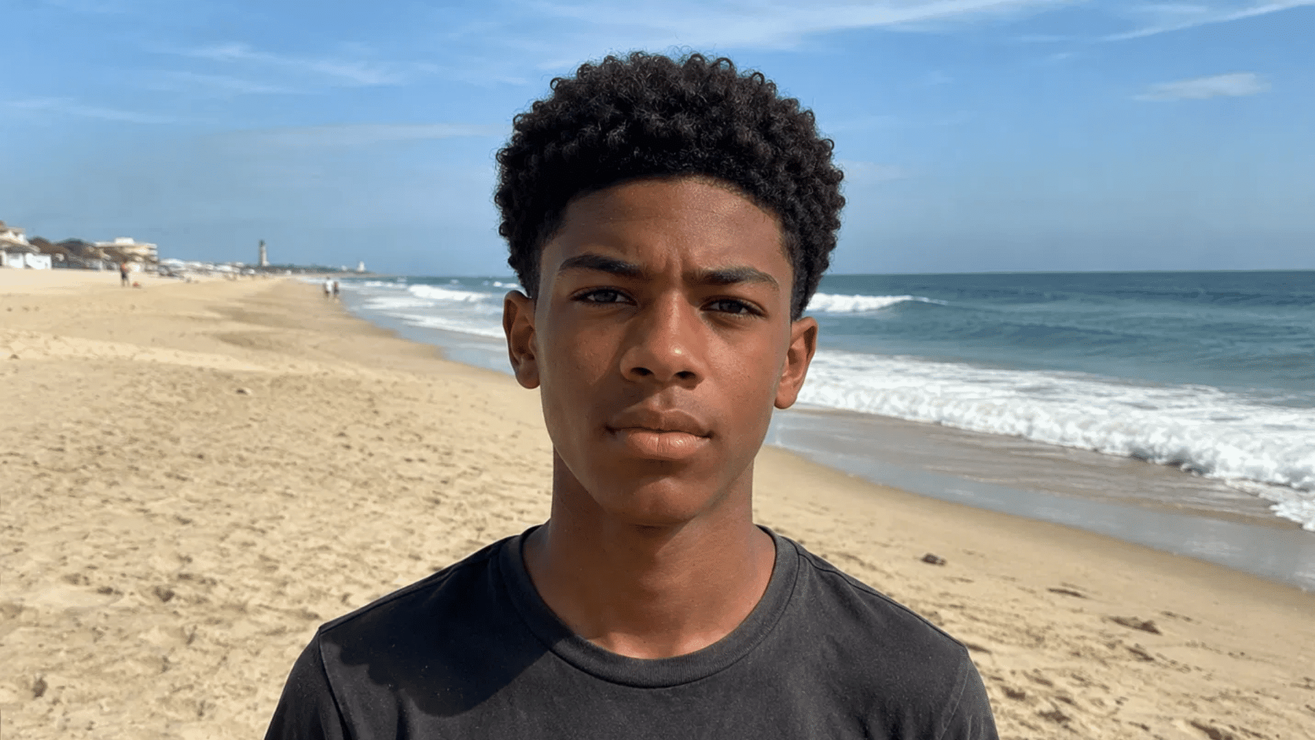 teenager with curly crew cut natural texture hairstyle standing on sandy beach shoreline