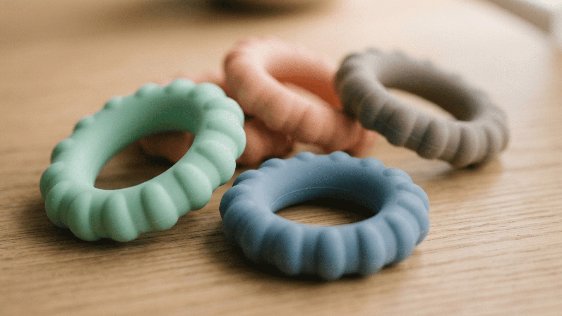 four soft silicone grip rings in muted colours with ridged textures on a wooden surface