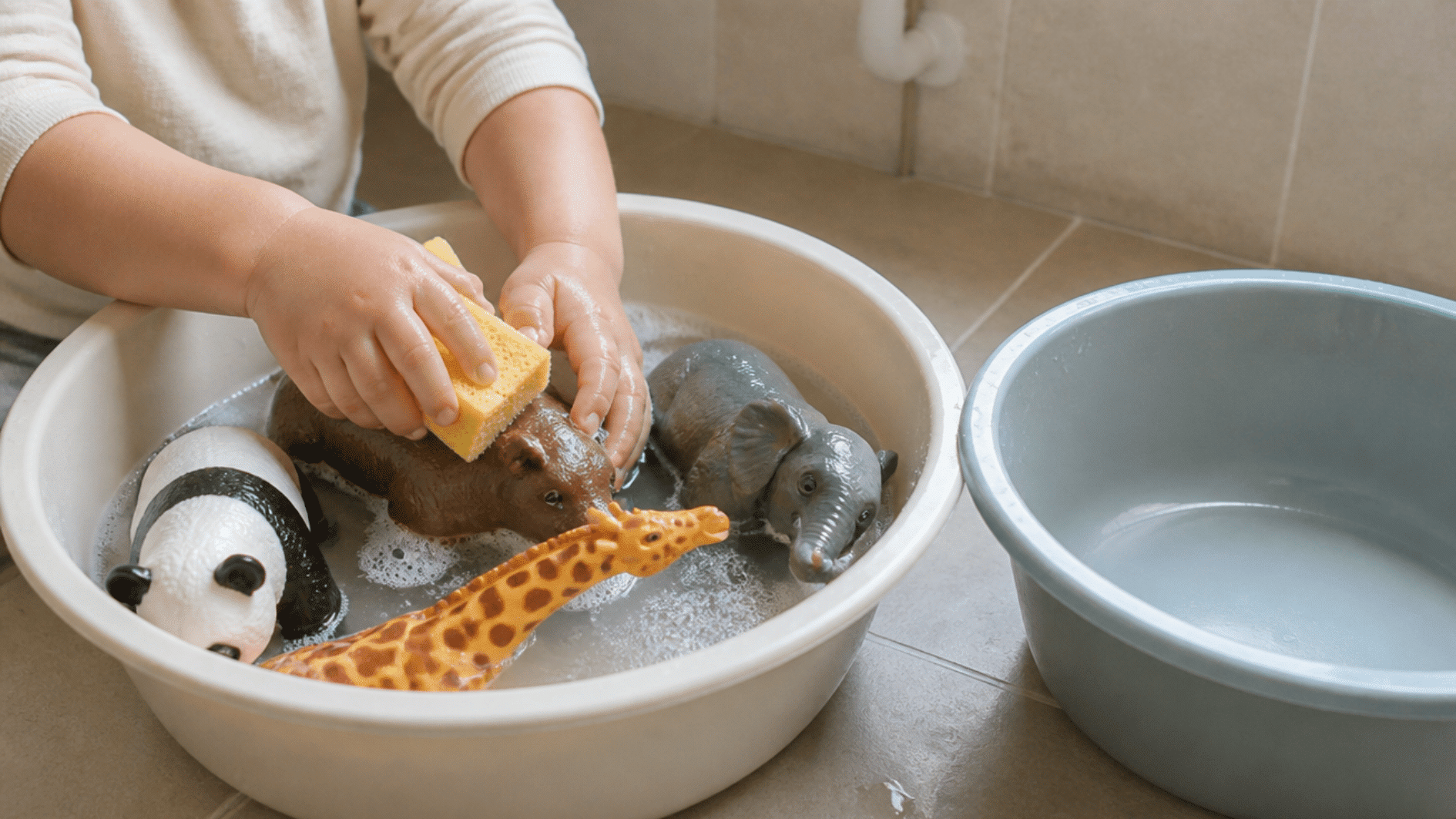 toddler washing large toy animals with a sponge in a shallow basin during sensory play