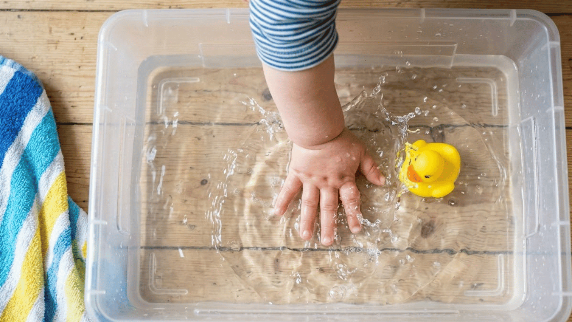 toddler hand splashes in a shallow bin of water with a floating toy nearby
