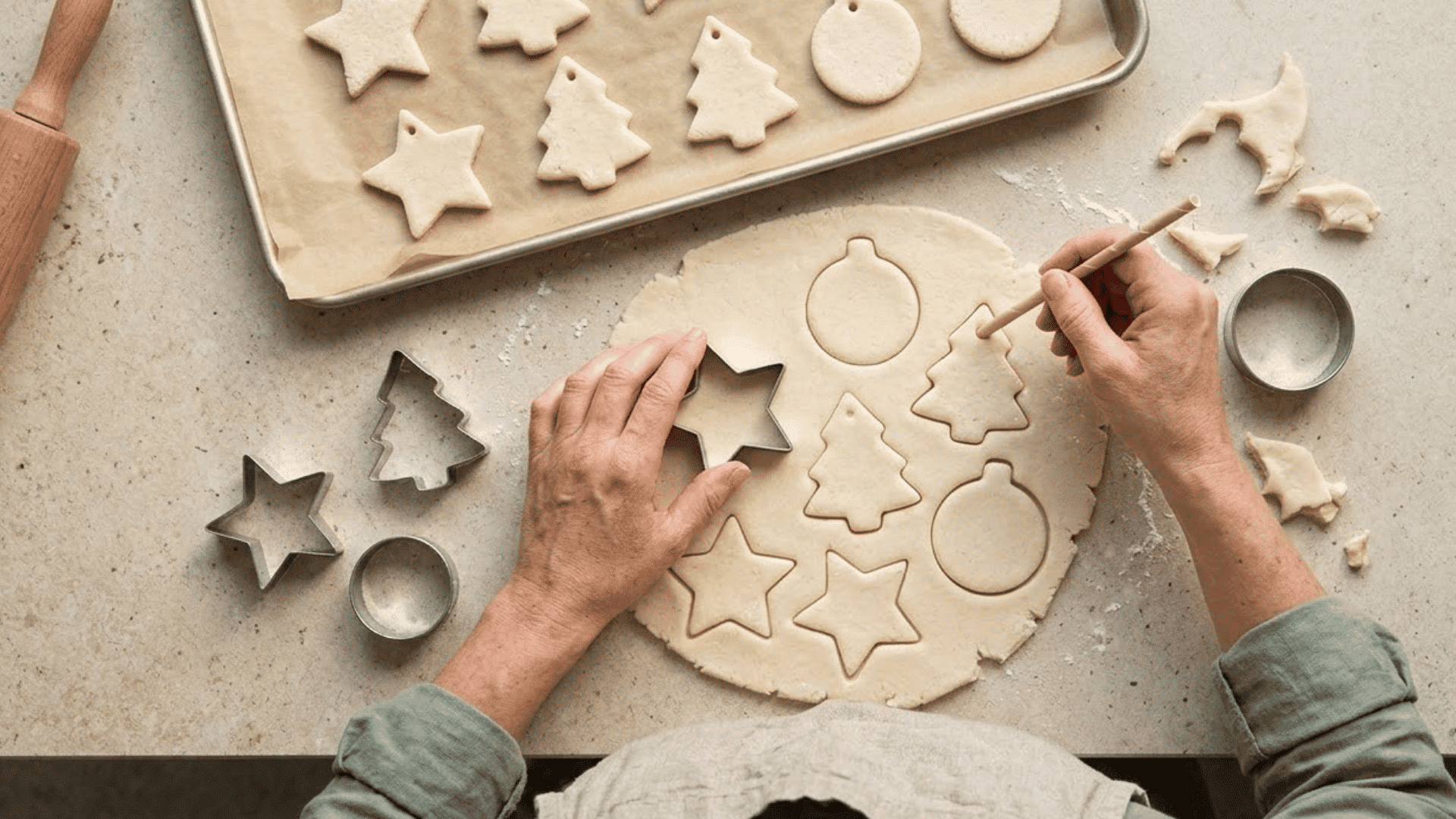 woman cutting salt dough shapes and adding hanging holes before placing them on a lined baking sheet