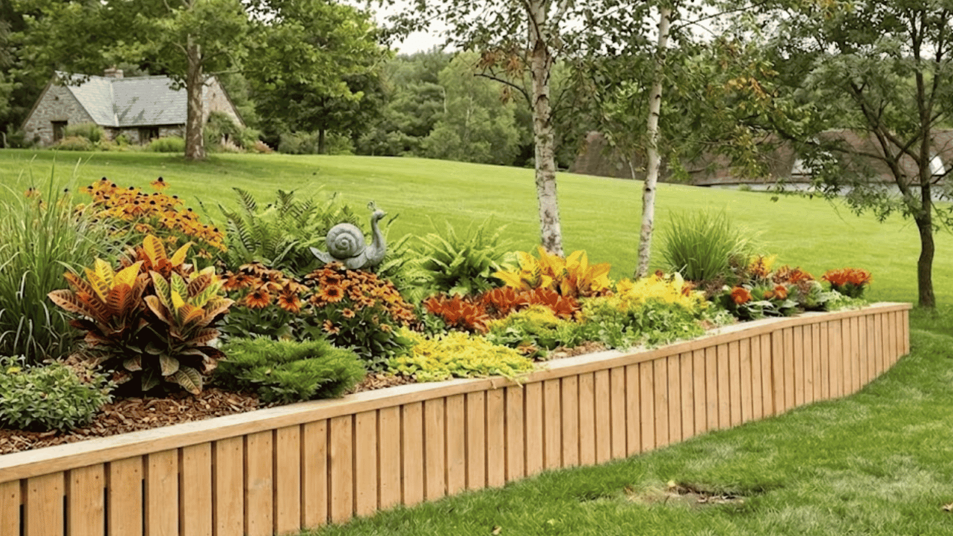 wood retaining wall garden bed filled with colorful flowers and plants across a large green backyard