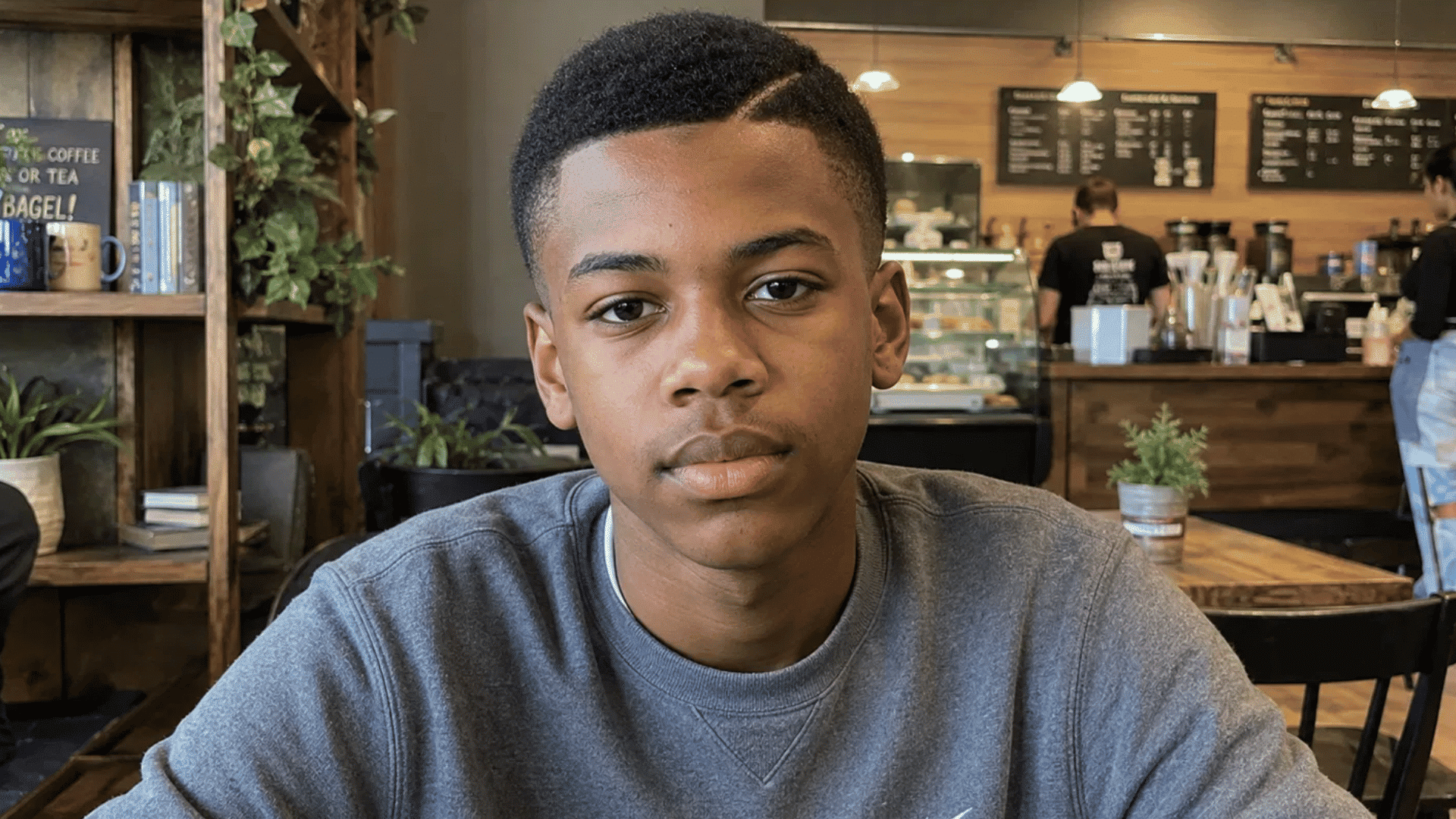 young man sporting crew cut with natural part hairstyle sitting inside cozy coffee shop cafe