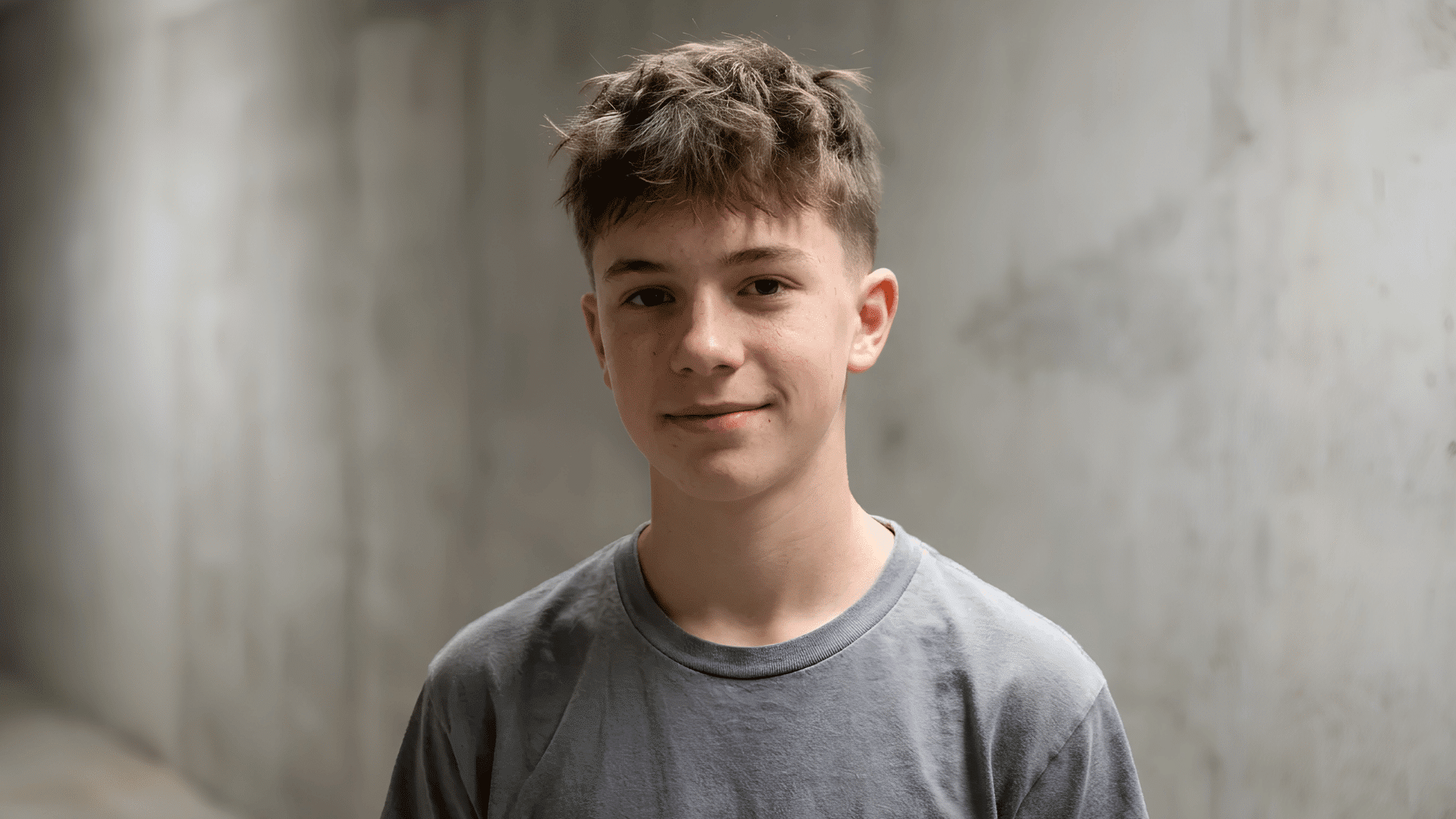 young teen smiling with messy textured top and faded sides haircut against blurred concrete backdrop