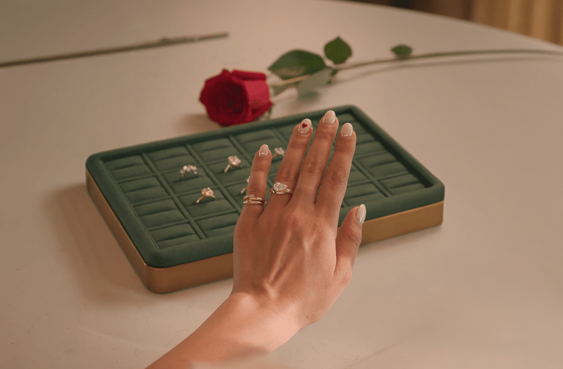 Hand displaying rings over green jewelry tray with rings, single red rose in background