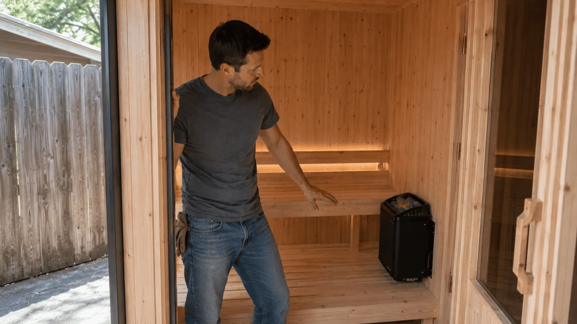 man inspecting the finished <echighlighted><echighlighted><echighlighted><echighlighted><echighlighted><echighlighted><echighlighted>diy sauna</echighlighted></echighlighted></echighlighted></echighlighted></echighlighted></echighlighted></echighlighted> interior with a glowing heater inside
