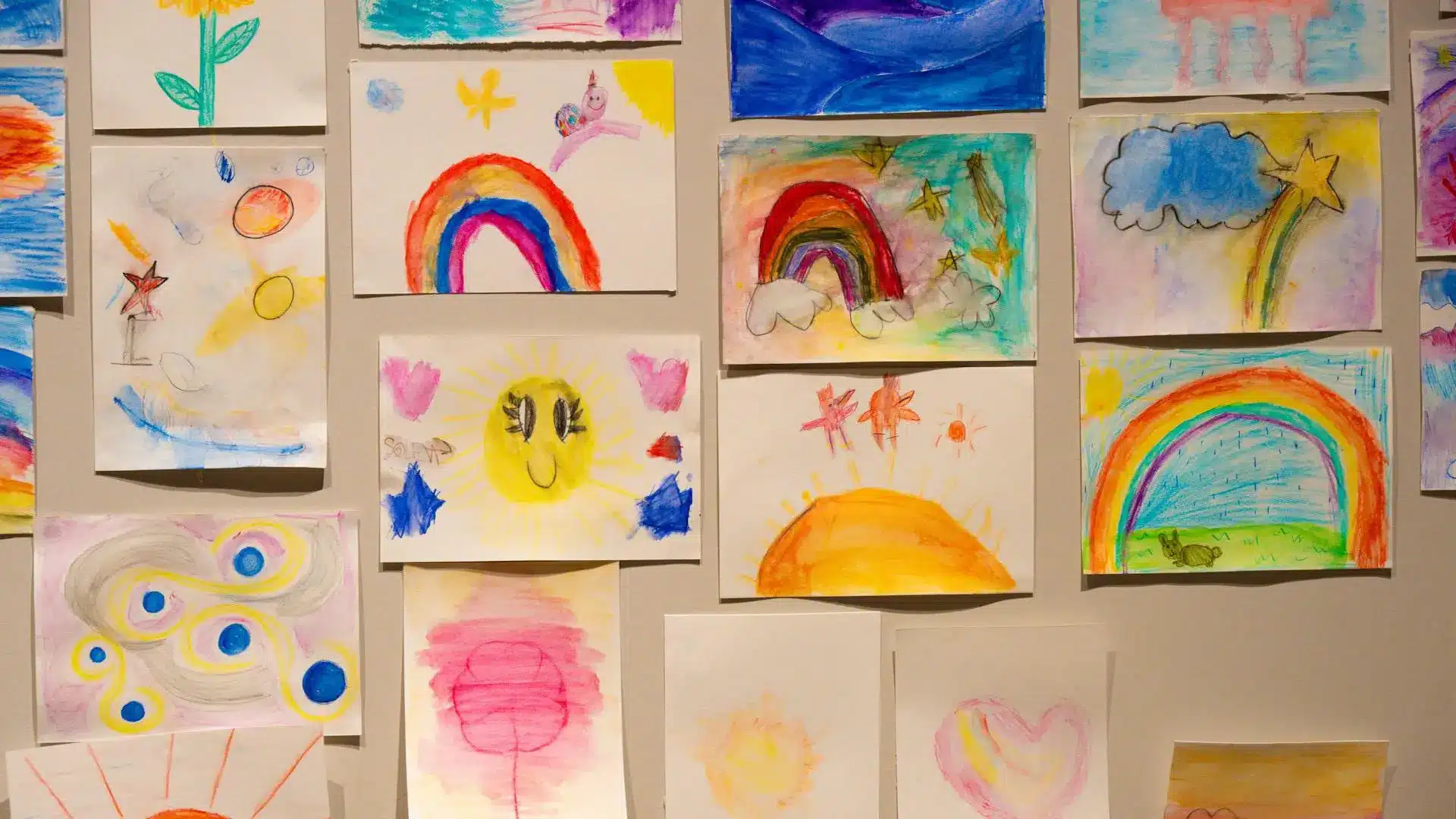 Children's colorful drawings of rainbows and suns displayed on a wall indoors
