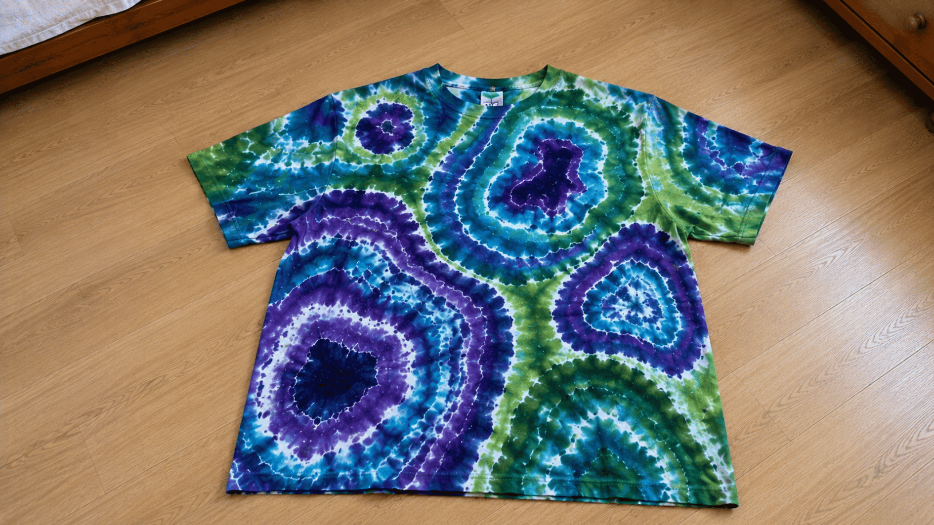 geode tie dye shirt with purple blue turquoise and green patterns laid on a light wooden floor