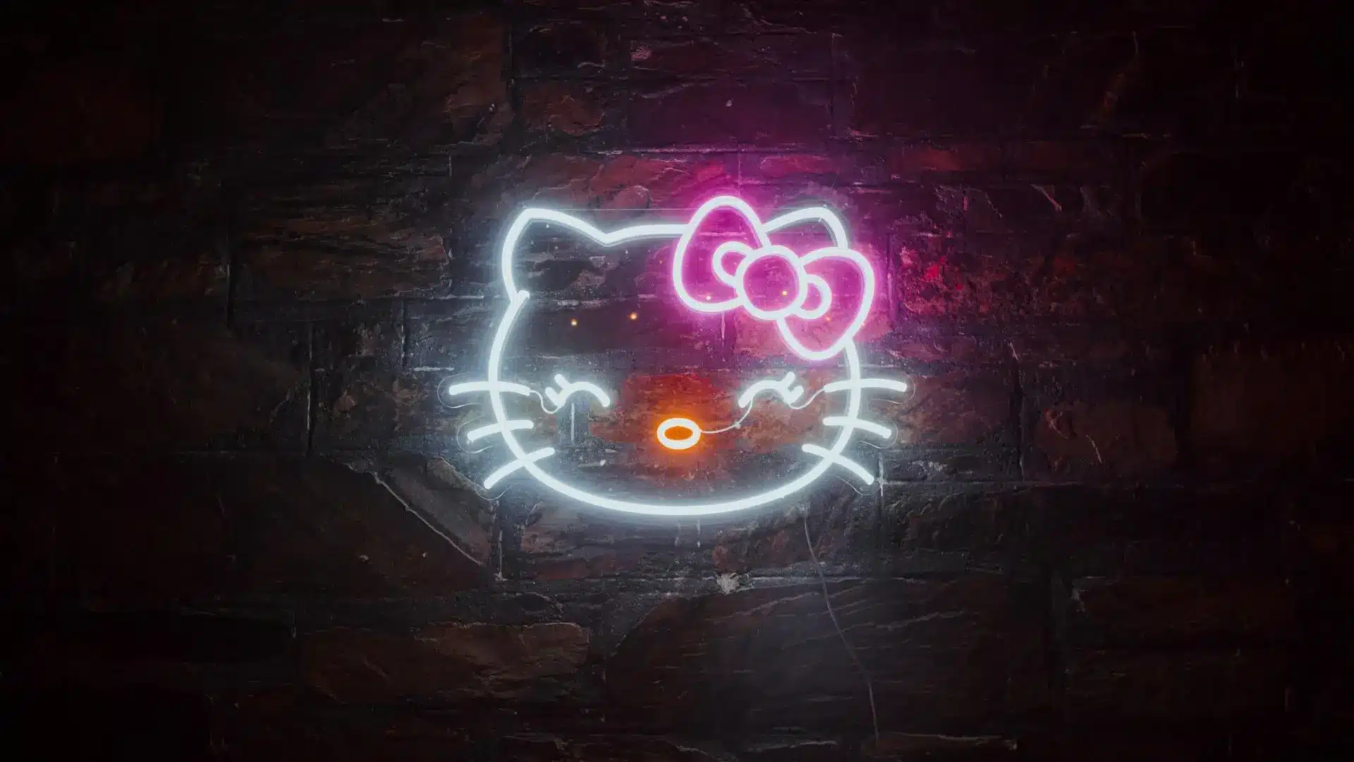 Neon sign of a cat face with bow on dark brick wall