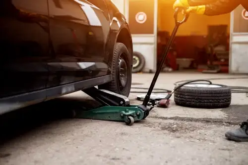 Car being lifted with hydraulic jack in garage setting with spare tire nearby