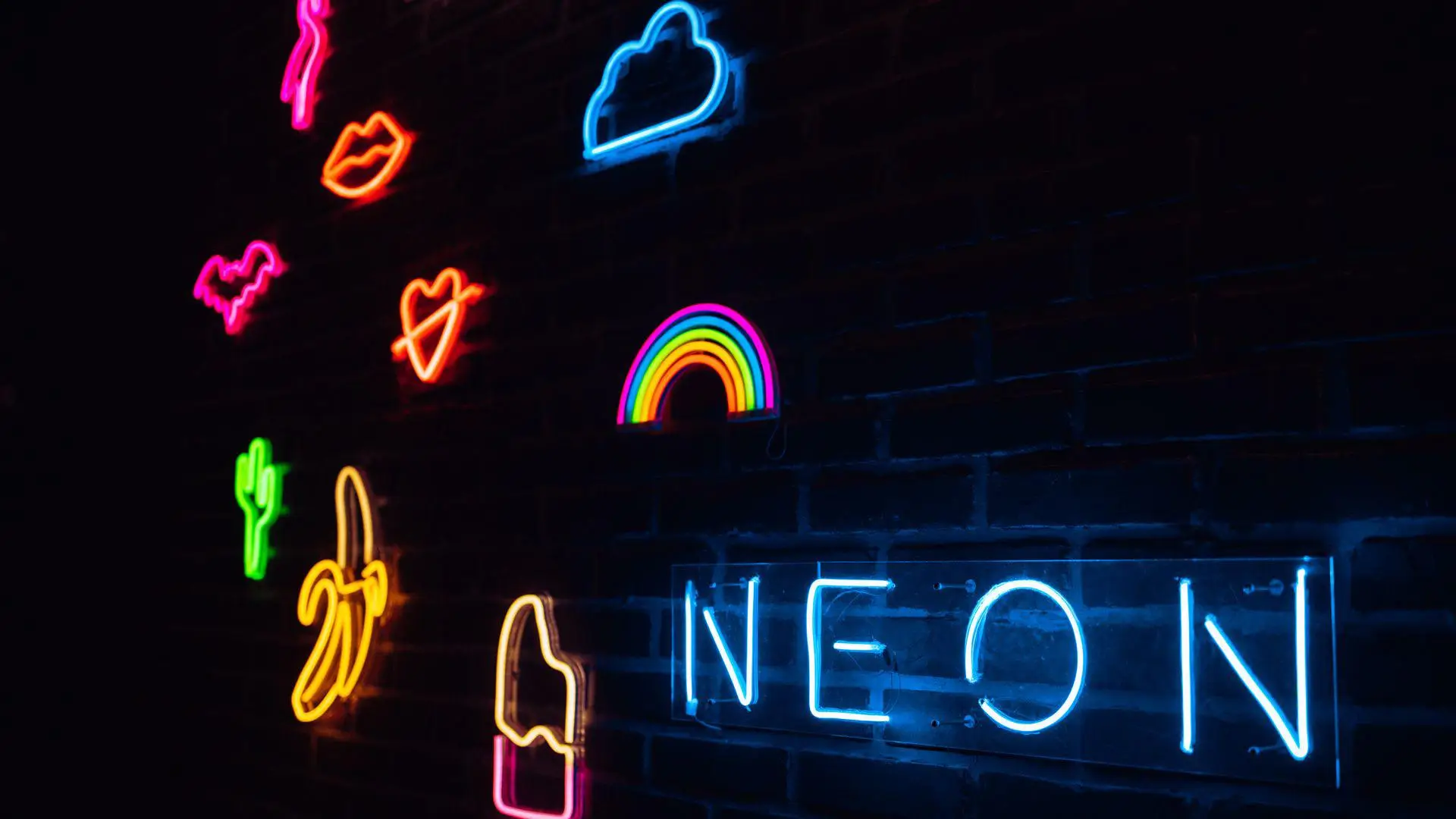 Colorful neon signs on a dark brick wall featuring cloud, rainbow, and various symbols