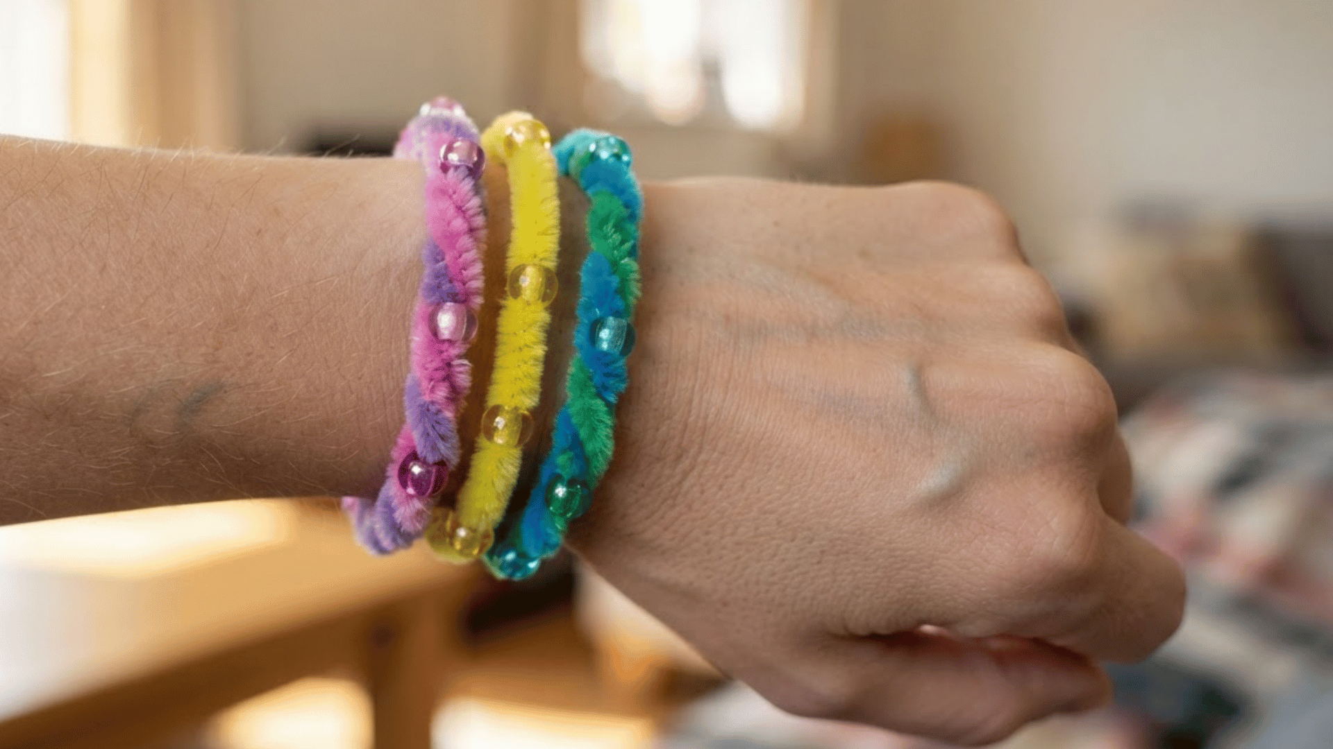 colorful beaded pipe cleaner bracelets in pink yellow blue and green worn together around a wrist in soft indoor light