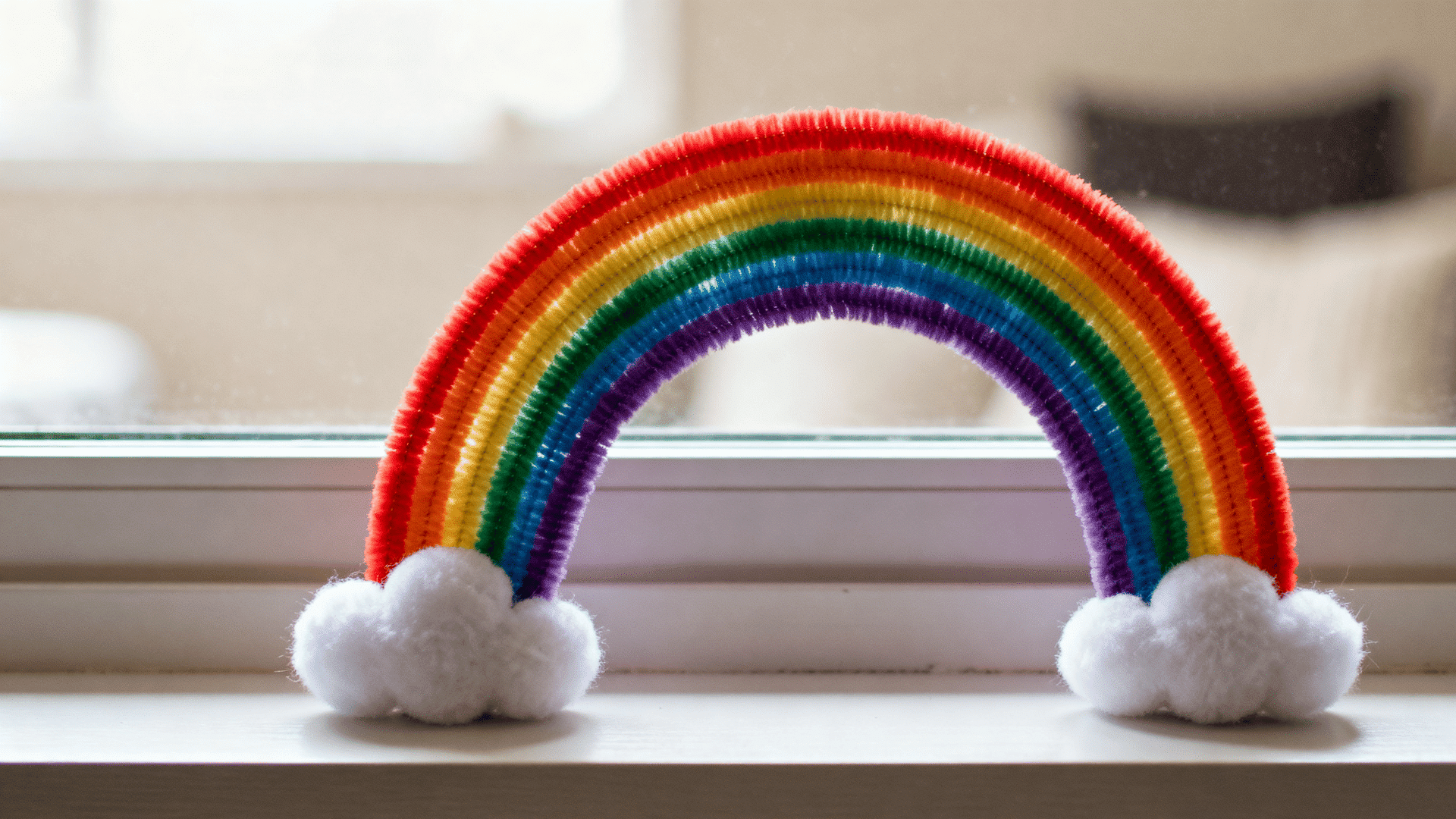 rainbow made from red orange yellow green blue and purple pipe cleaners with white clouds on a windowsill indoors