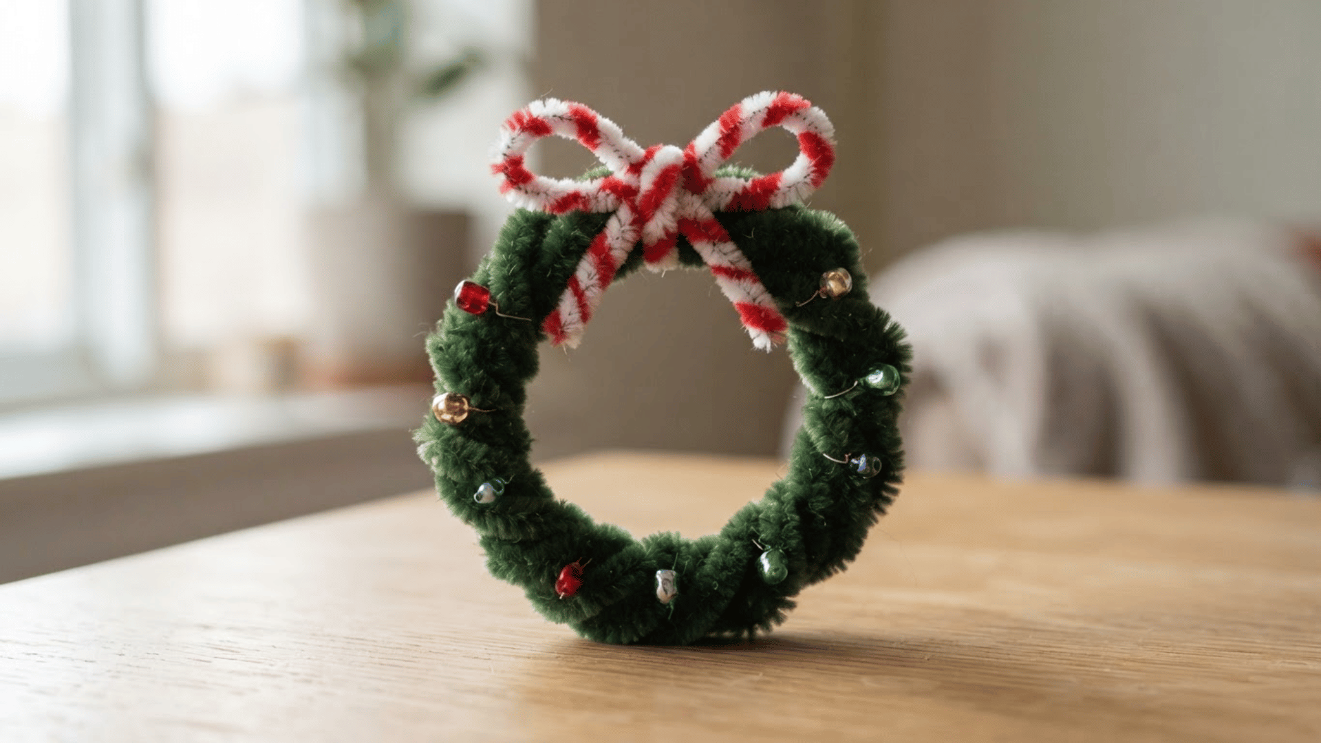 green pipe cleaner wreath with colorful bead accents and a red and white striped bow displayed on a wooden table
